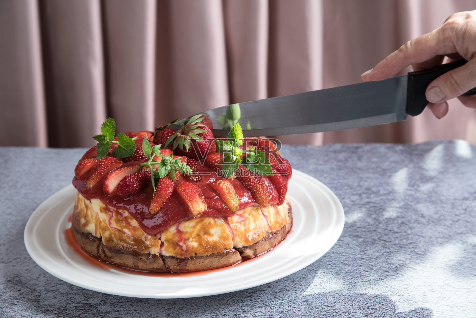 一个女人用刀切着自制的草莓派。夏季甜点的概念照片摄影图片