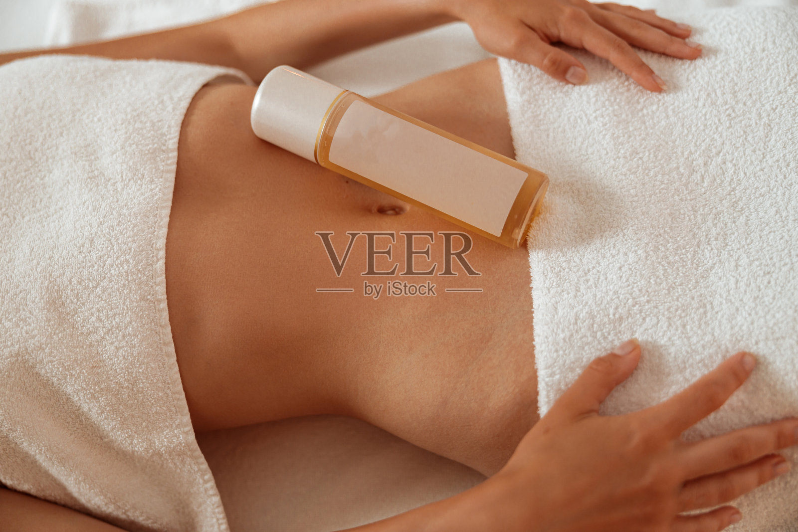 年轻的女人与化妆品在她的腹部休息在水疗沙龙照片摄影图片