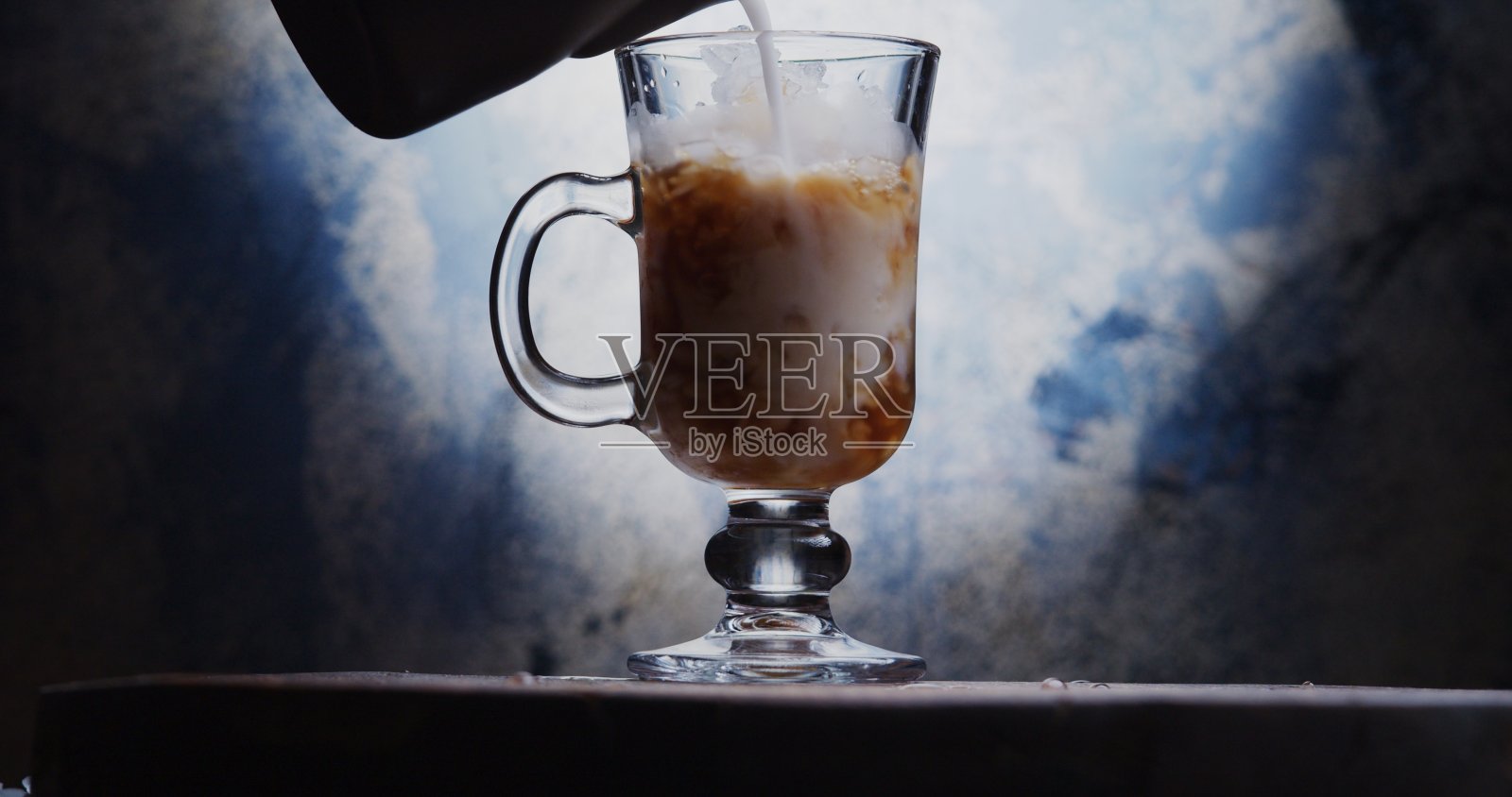 往爱尔兰玻璃杯里倒牛奶,杯子里装满了冰咖啡和碎冰照片摄影图片