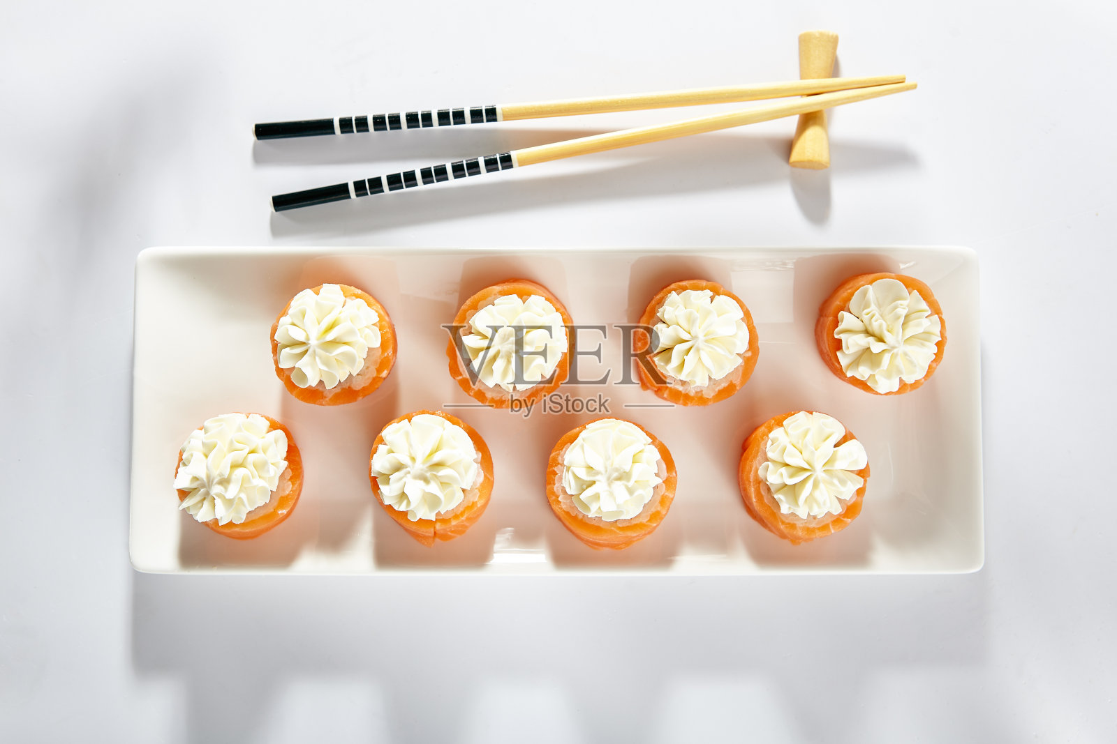 费城寿司卷由烟熏三文鱼制成。奶油芝士寿司。白色的盘子和木筷子放在白色的桌子上。照片摄影图片