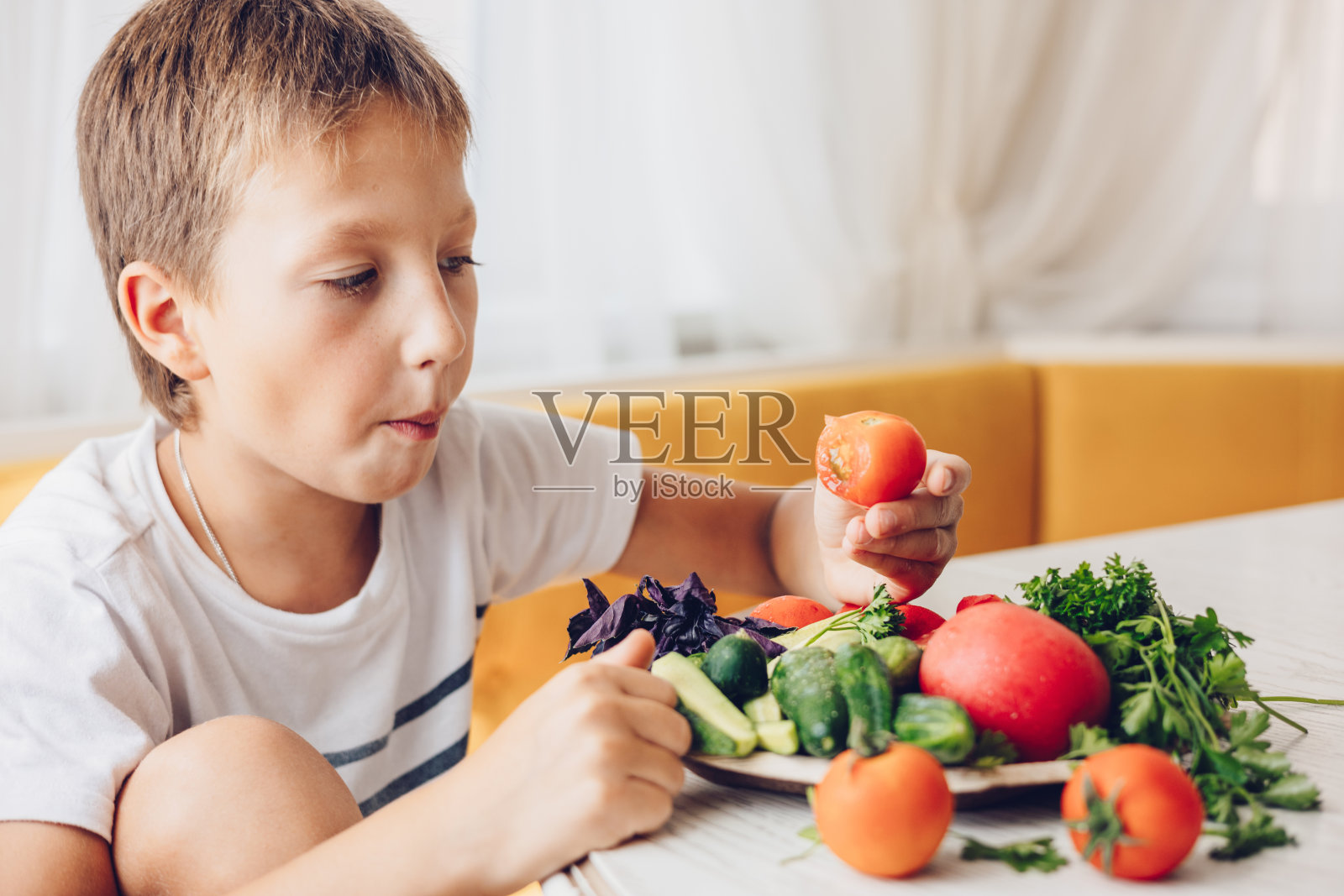 男孩坐在厨房里吃着健康的蔬菜黄瓜和西红柿照片摄影图片