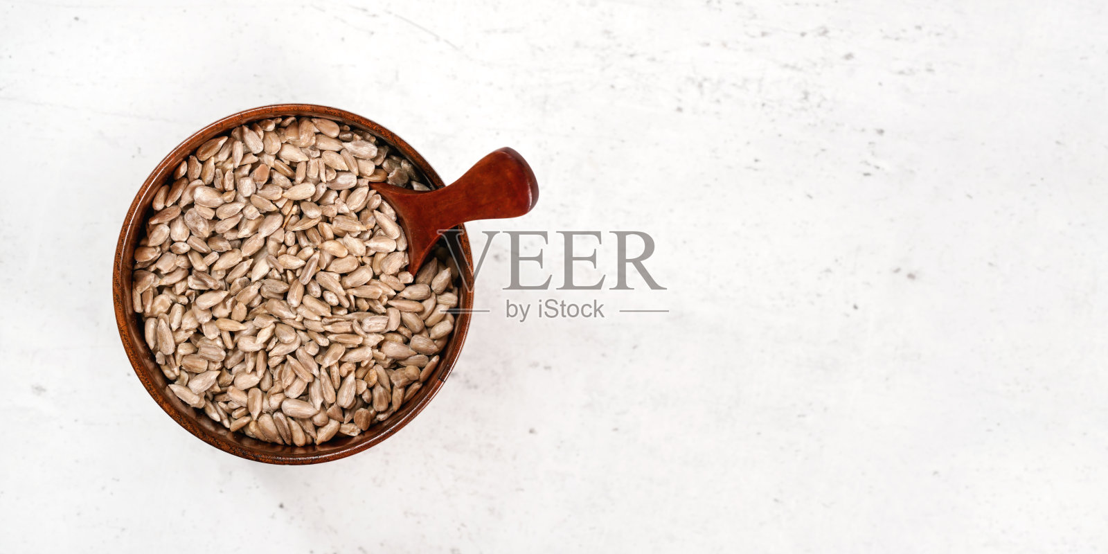 将去皮的葵花籽放入小木杯中,用小勺放置在白色石头状的木板上,从上面看,右侧宽大的横幅空间为文字照片摄影图片