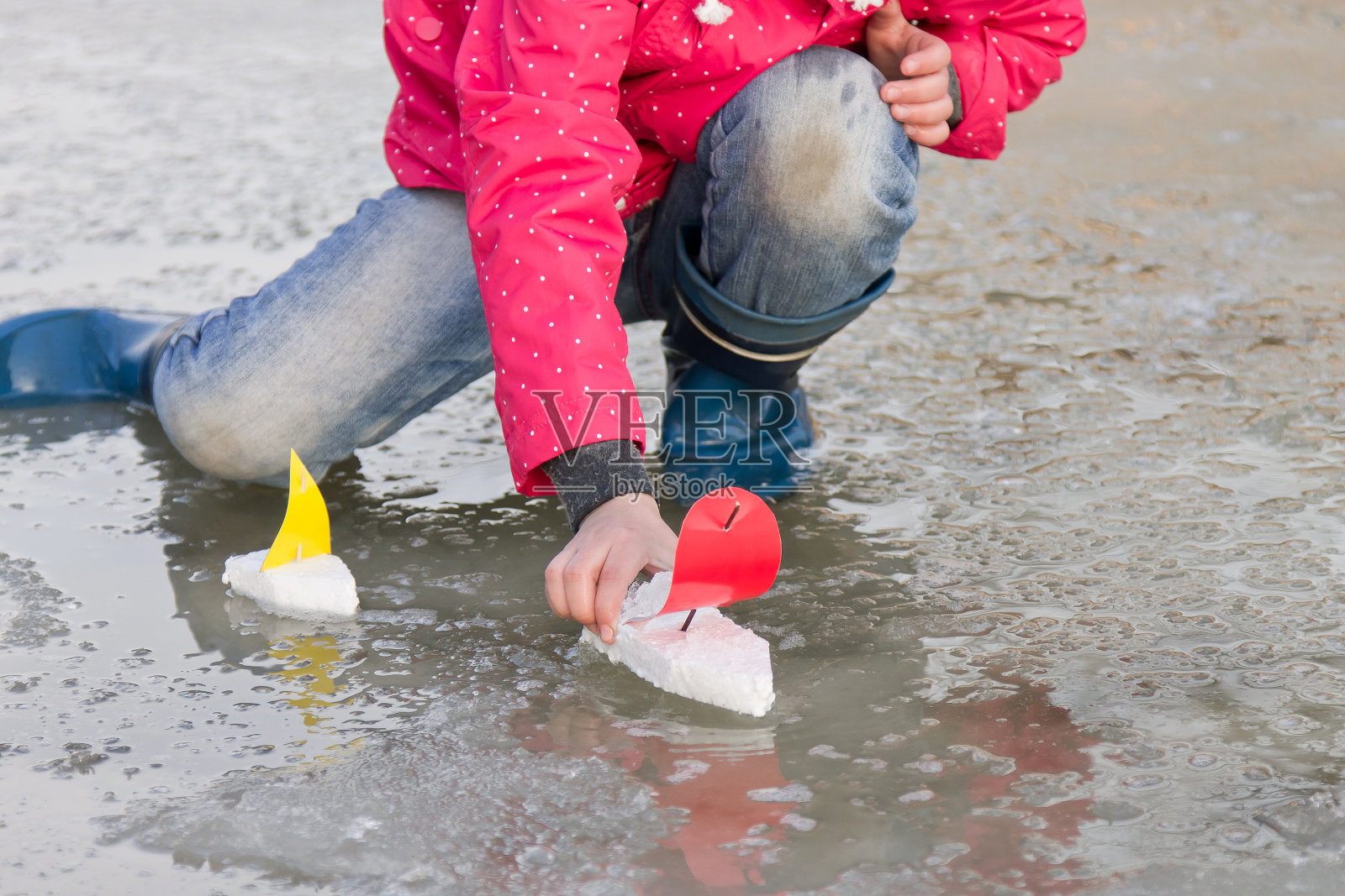 小女孩穿着雨靴在泉水坑里玩玩具船照片摄影图片