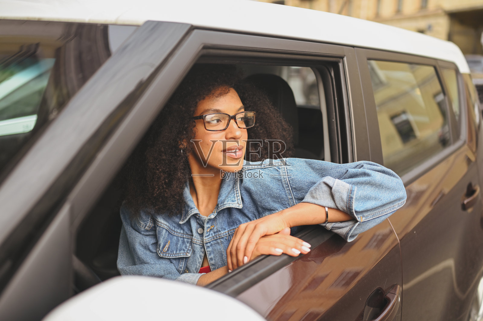 快乐的年轻微笑的非洲裔美国女人黑头发戴眼镜的司机坐在新的棕色汽车,微笑着看着相机享受旅程。驾驶课程和人寿保险概念照片摄影图片