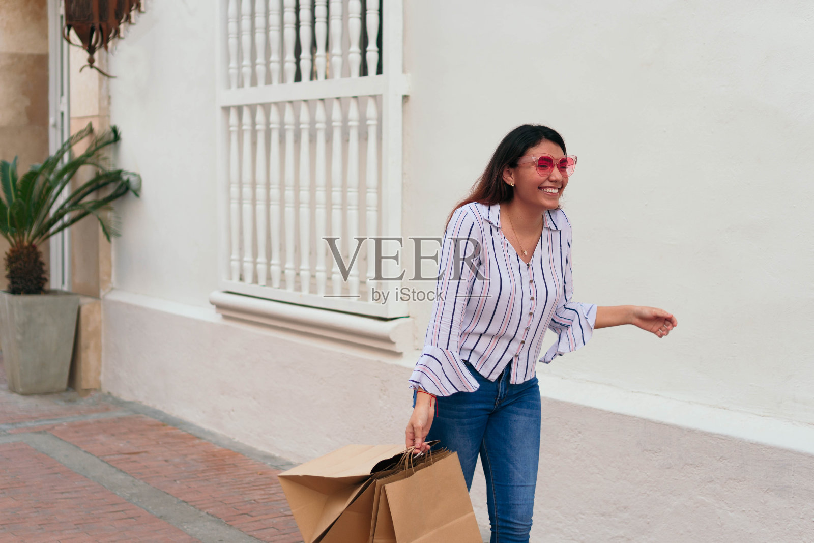 女人戴着太阳镜,提着购物袋站在墙边照片摄影图片