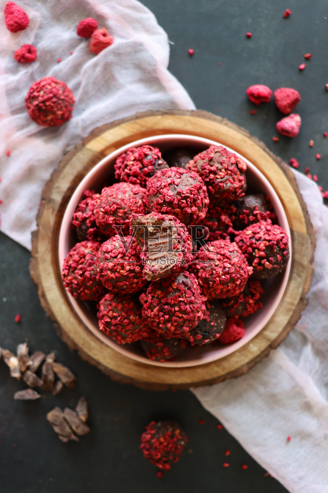 自制的巧克力松露糖果,以甘纳什为中心,堆在木板上的粉红色碗里,奢华的巧克力球涂上脱水的覆盆子,粉红色的平纹布,没有咬痕,深灰色的背景,高架的视野照片摄影图片