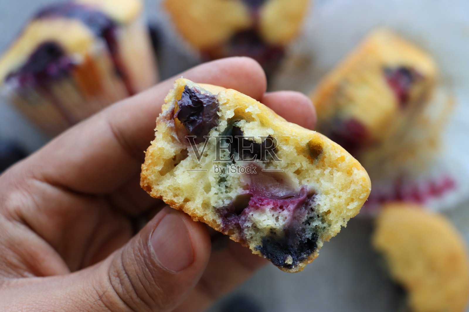 特写图像,一个不认识的人拿着一个自制的蓝莓松饼在一堆蛋糕上,有纹理的灰色背景,高架视野照片摄影图片