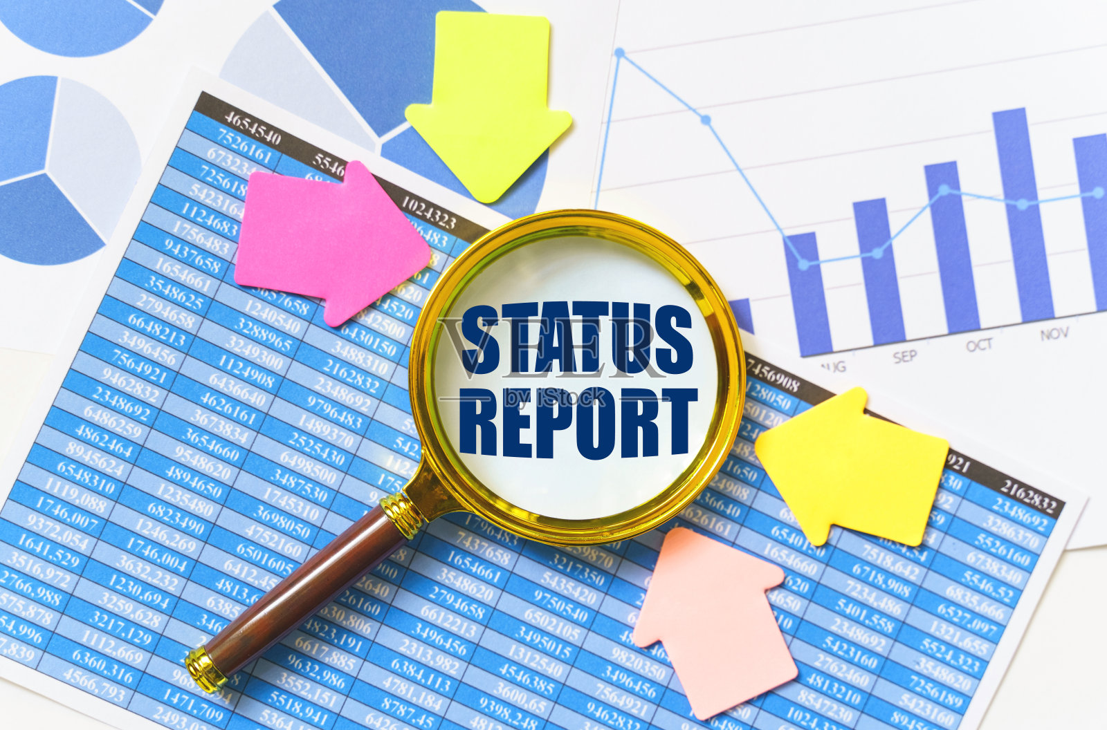 桌子上放着财务报告、图表和一个放大镜,放大镜里面刻着“现状报告”照片摄影图片