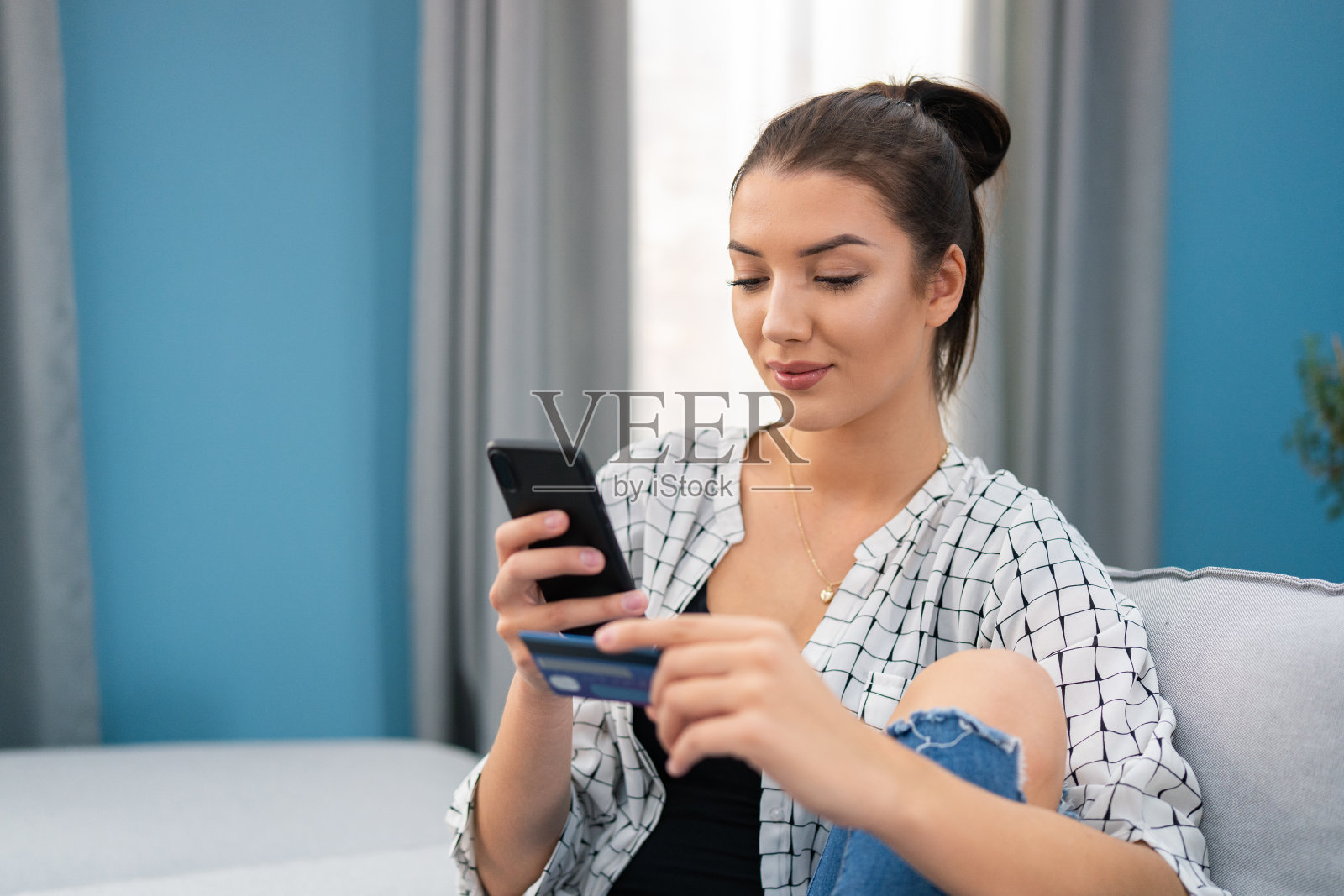 一个喜欢购物的年轻女人坐在家里的沙发上浏览交易,寻找促销,从网上商店买衣服,手袋,饰品,她很满足,很开心照片摄影图片