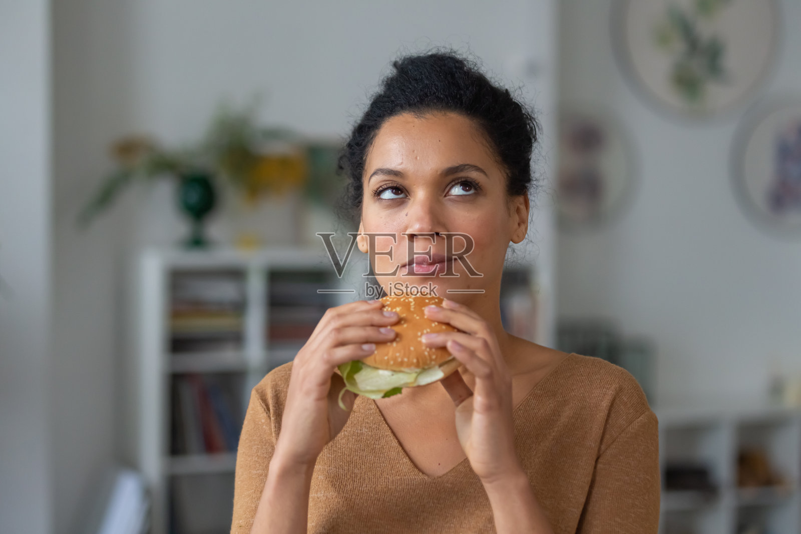 漂亮的非裔美国女人的肖像,胃口大开,喜欢咬汉堡。年轻的混血女性吃着快餐,在光线模糊的背景下摆着姿势。近距离照片摄影图片