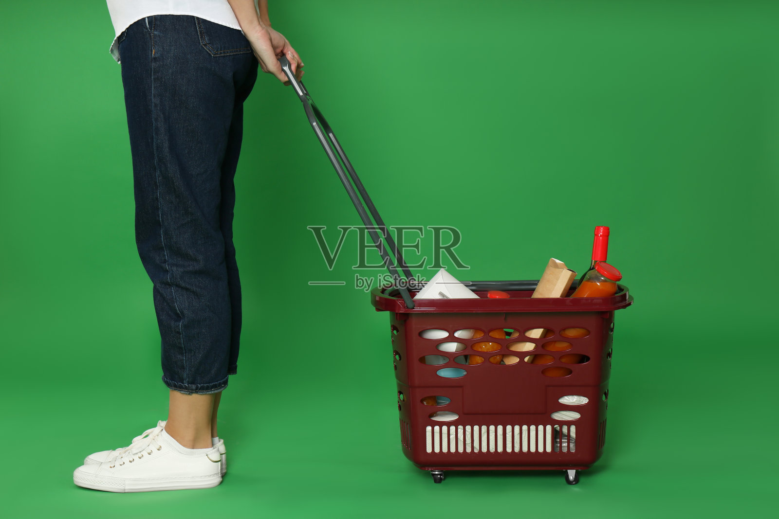 绿色背景上,女人拿着装满不同产品的购物篮,特写照片摄影图片