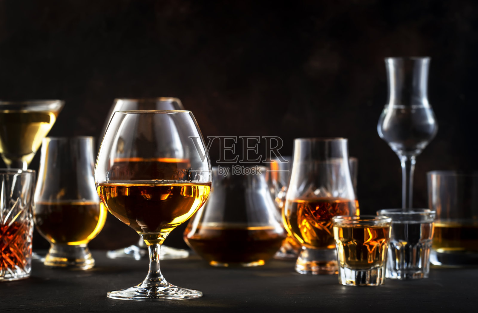 烈性酒、烈酒和蒸馏物放在玻璃杯里:干邑白兰地、苏格兰威士忌和其他。黑条计数器背景照片摄影图片