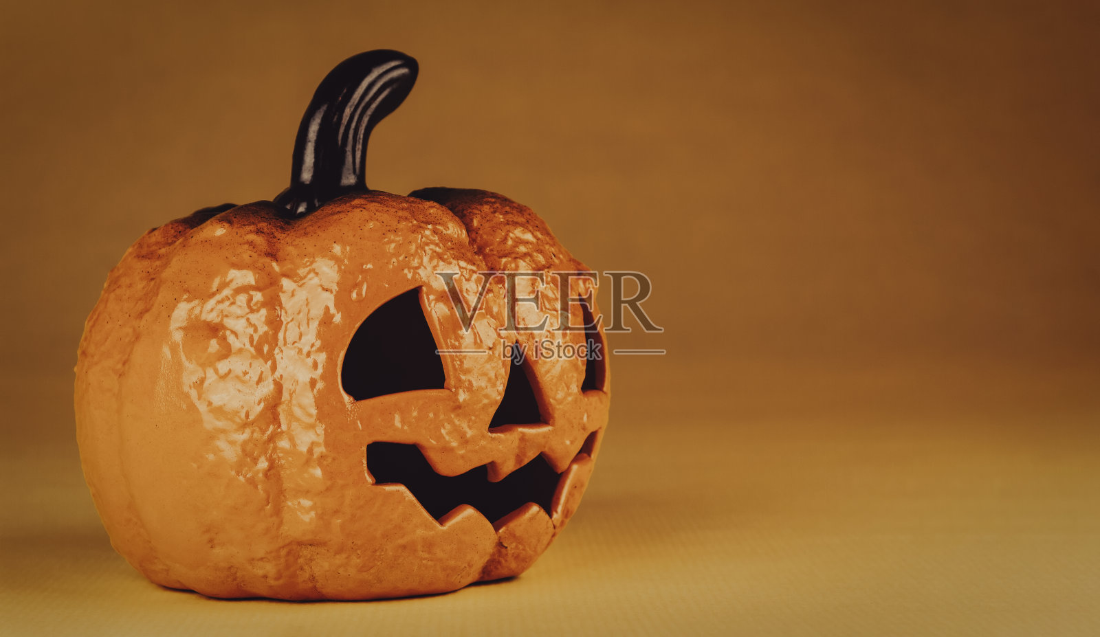 陶瓷南瓜与幽灵的脸在万圣节的夜晚在橙色的背景与复制空间照片摄影图片