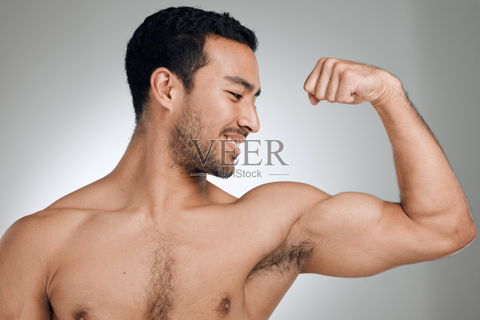 一名年轻男子站在灰色背景下展示肌肉照片摄影图片