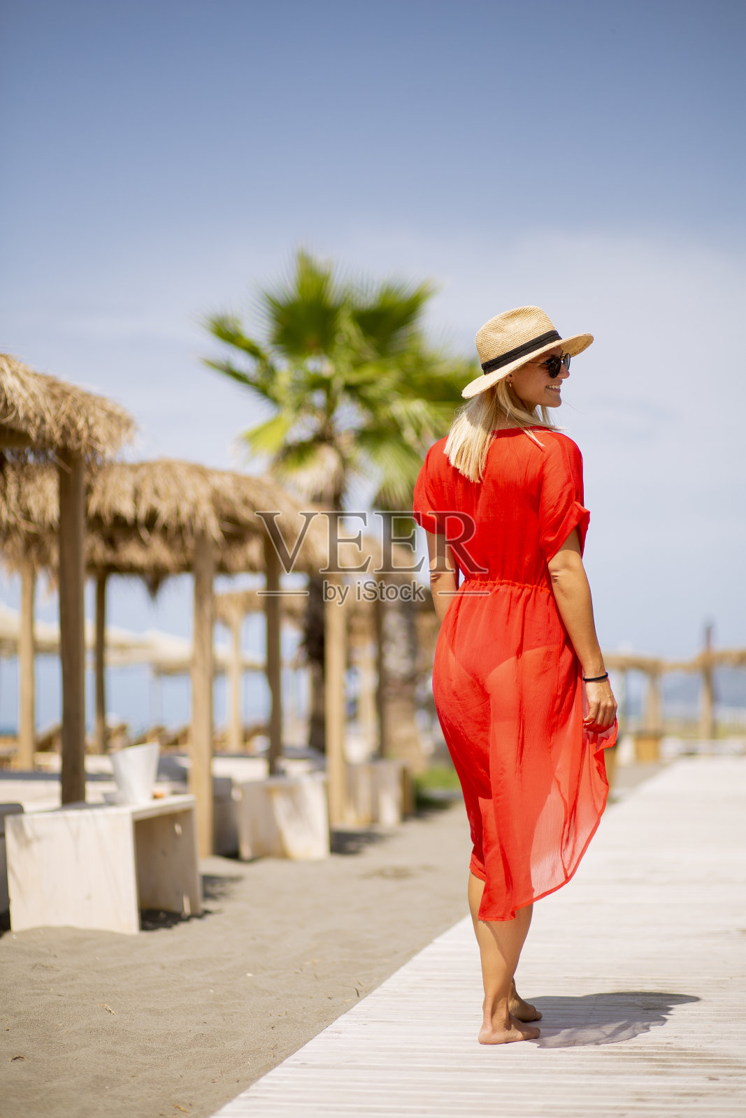 夏天,一名身穿红色连衣裙的年轻女子在海滩上散步照片摄影图片