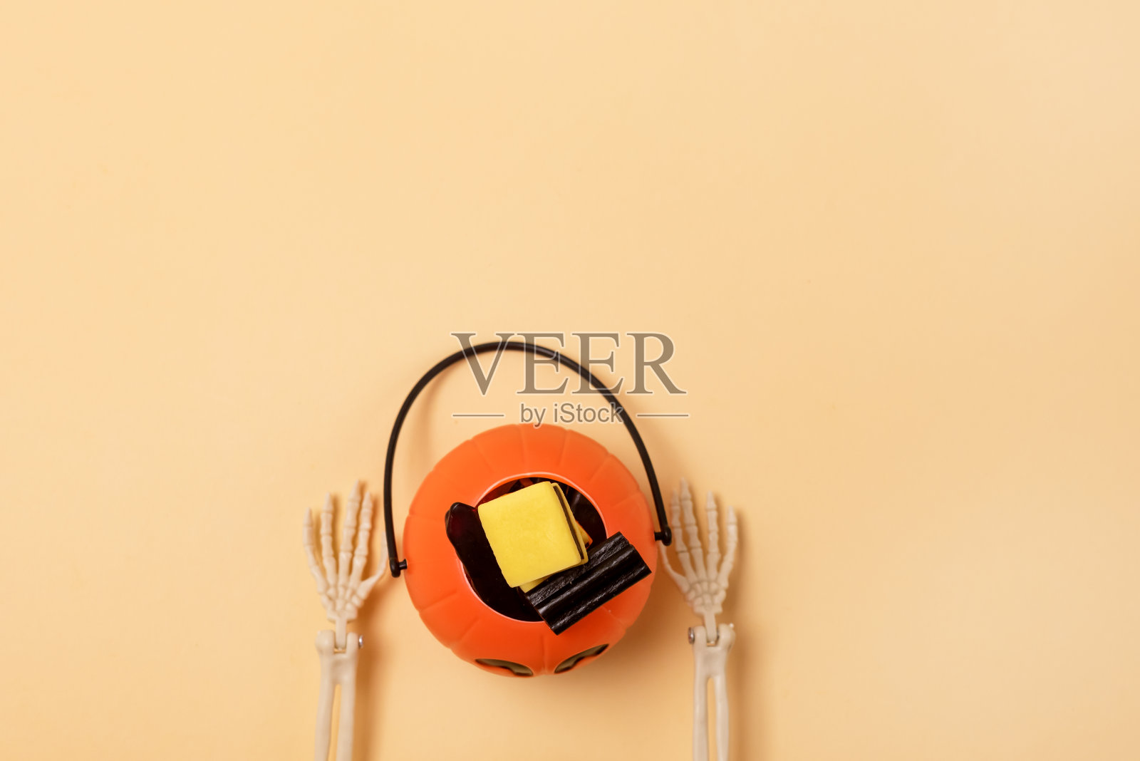 骷髅手臂手持小南瓜灯南瓜篮与糖果黄色背景顶部视图复制空间照片摄影图片