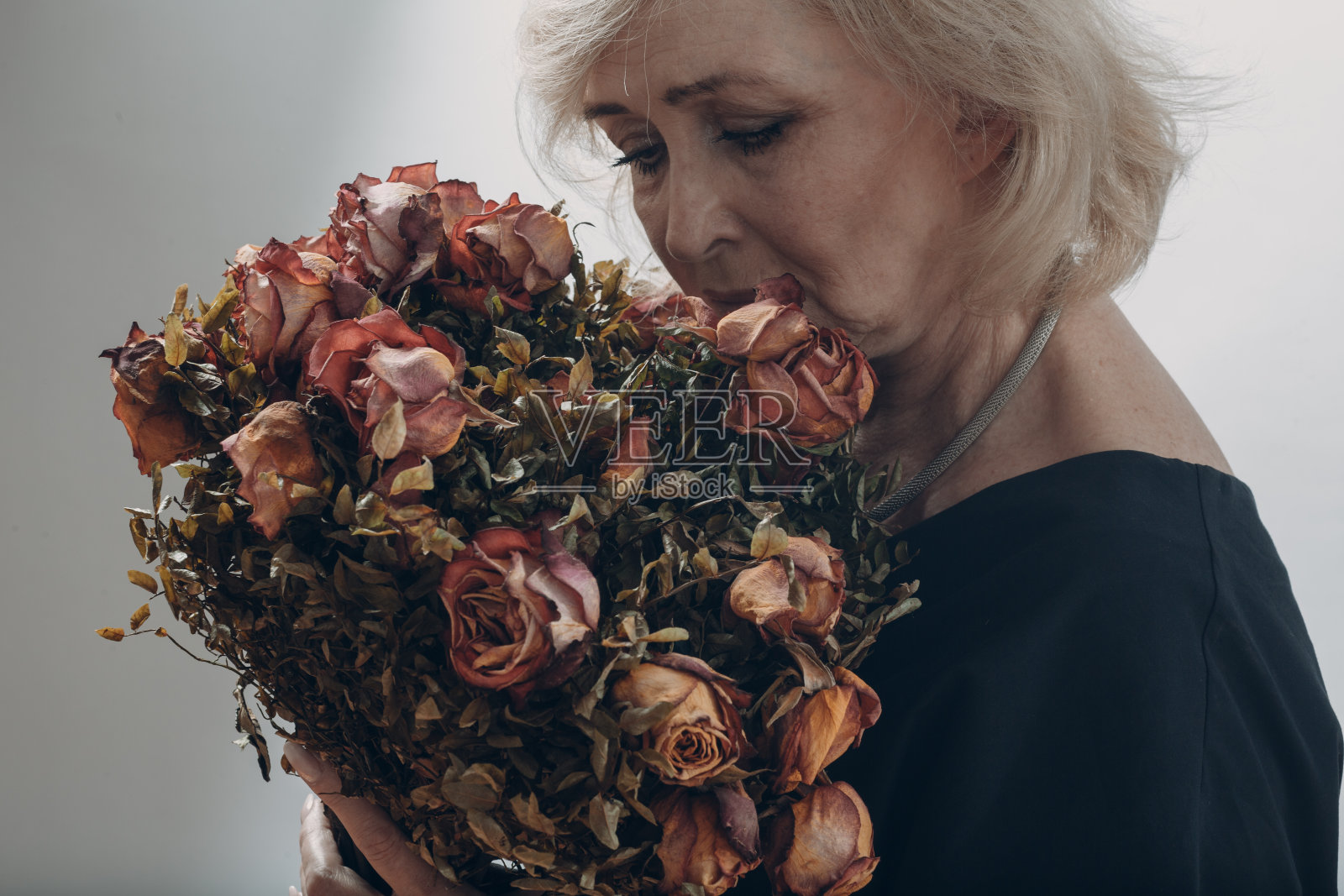 心烦意乱的老妇人捧着干枯的老玫瑰花束。照片摄影图片