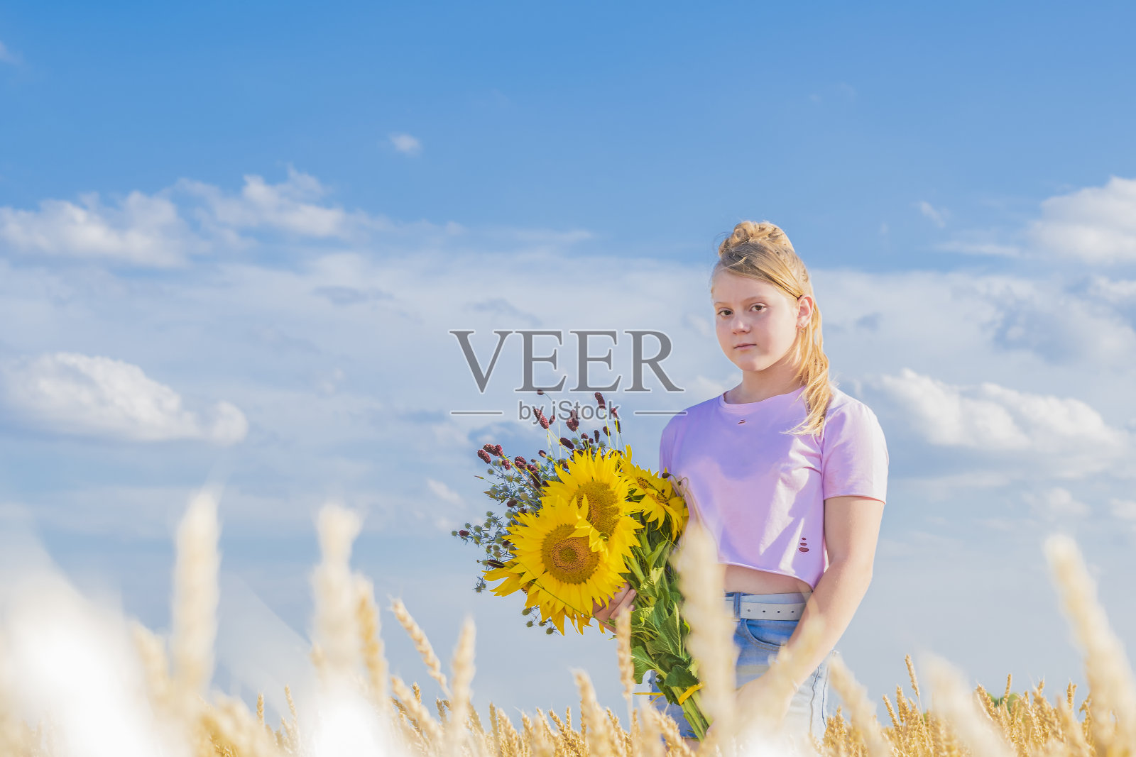 快乐的少女手捧一束向日葵和野花,在夏日蔚蓝的天空中摇曳。照片摄影图片