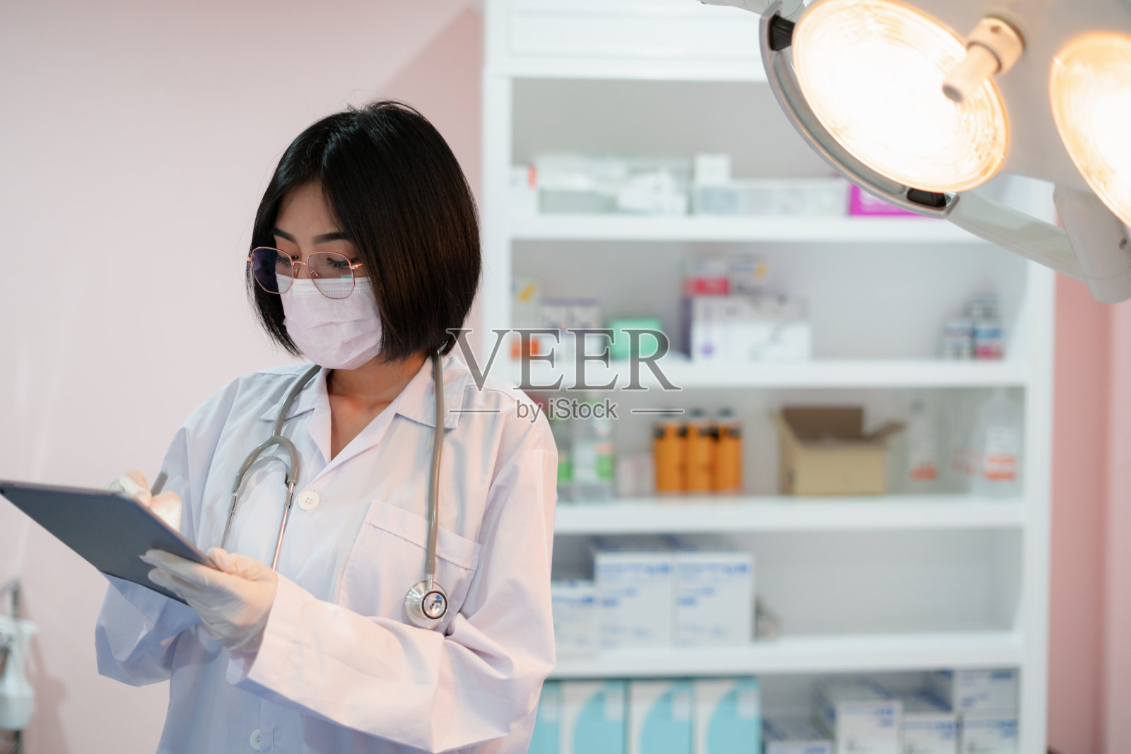 手术室里,医生戴着防护口罩,亚洲女性穿着白色制服,脸上挂着白色的东西。照片摄影图片