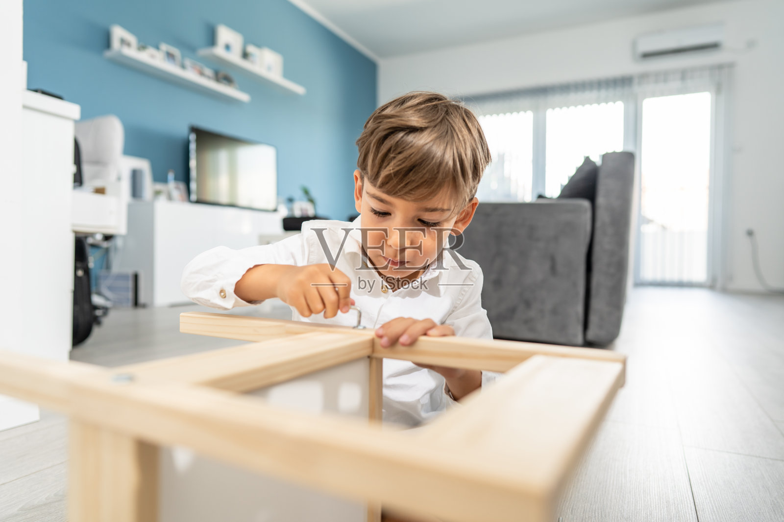 小白种人男孩在家里的地板上玩自己组装的椅子或桌子在白天-小孩子组装家具独自童年工艺概念前视图复制空间照片摄影图片