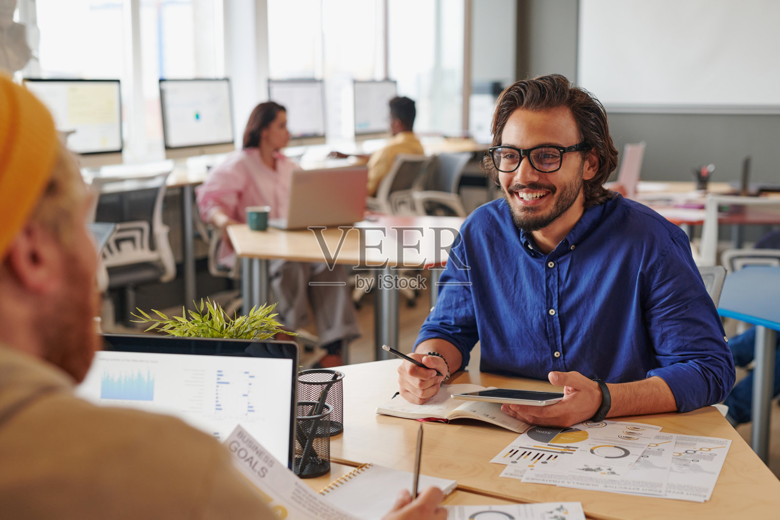 积极的年轻人坐在桌子上与文件和讨论项目在共同的工作空间照片摄影图片