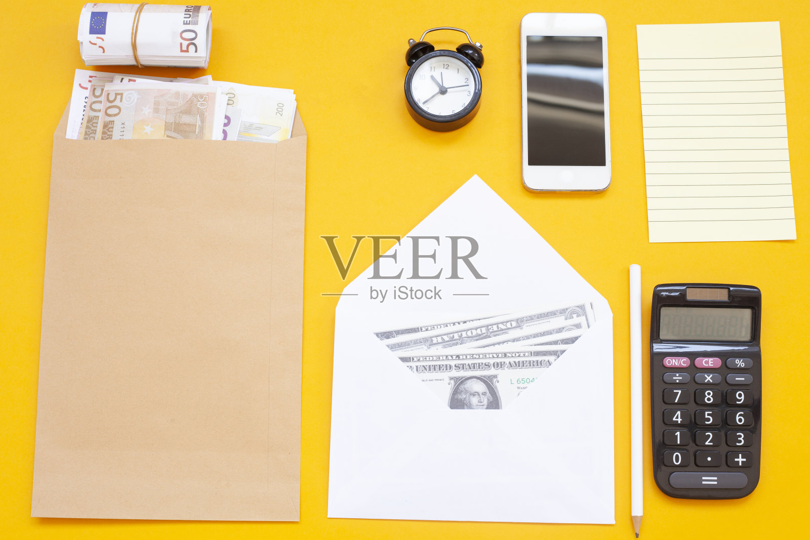 美元和欧元在信封上的黄色背景,笔记纸,笔,键盘,鼠标,电话,闹钟,商业设计在黄色背景照片摄影图片