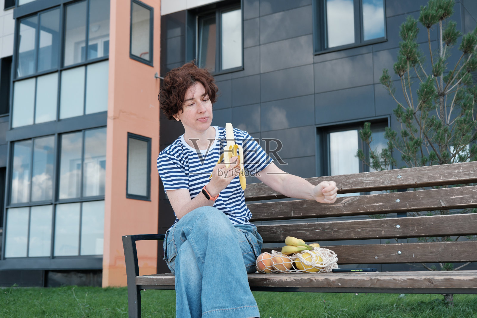 一位妇女坐在长凳上,手里拿着装在可重复使用的棉花袋里的水果照片摄影图片