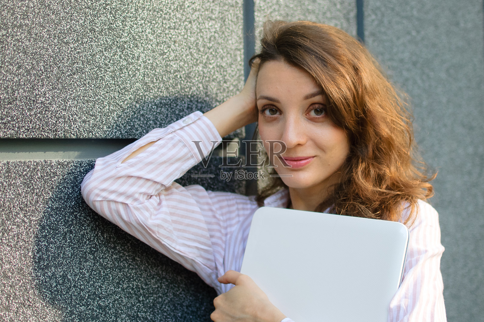 一名年轻女子的照片,手持银色笔记本电脑,一名女商人在工作间隙等待开会时,手持数码平板电脑,背景是深色的墙壁照片摄影图片