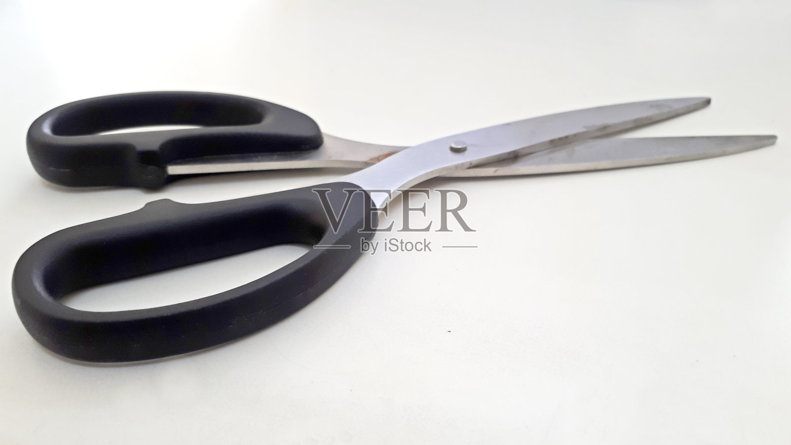 在一张白色的木桌上,有一把黑色的不锈钢大剪刀,它非常锋利,可以剪纸和其他物品照片摄影图片