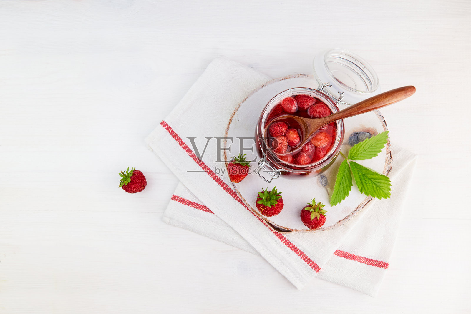 自制草莓酱,装在玻璃罐里,放在白色木板上。照片摄影图片