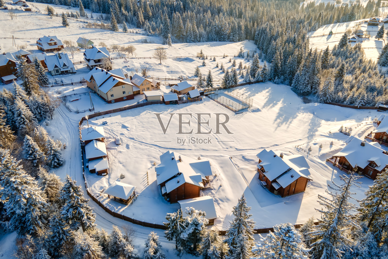 空中冬季景观与小村庄房屋之间的雪覆盖森林在寒冷的山在晚上。照片摄影图片