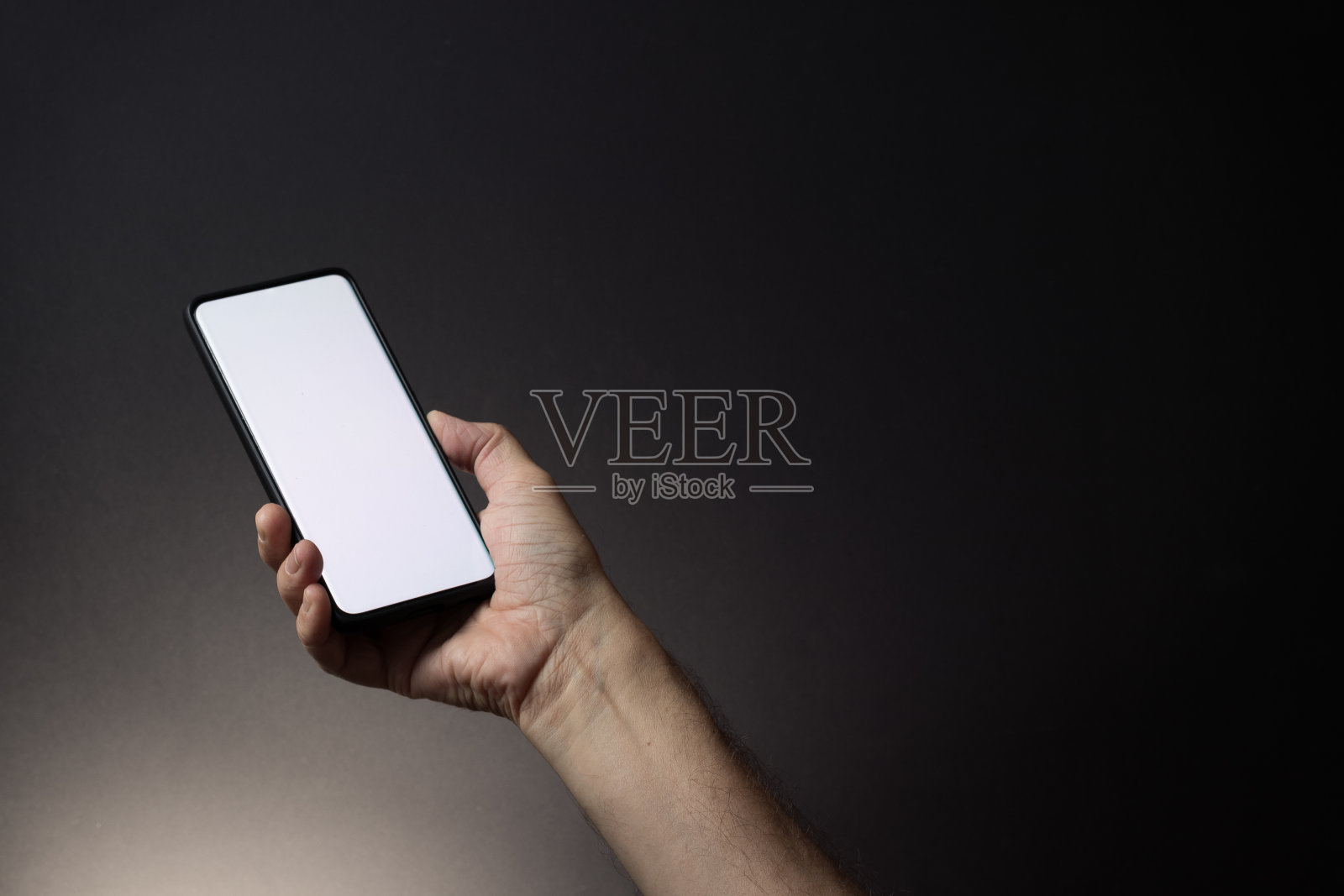 男子的手握黑色智能手机与空白的白色屏幕隔离在黑暗的背景照片摄影图片