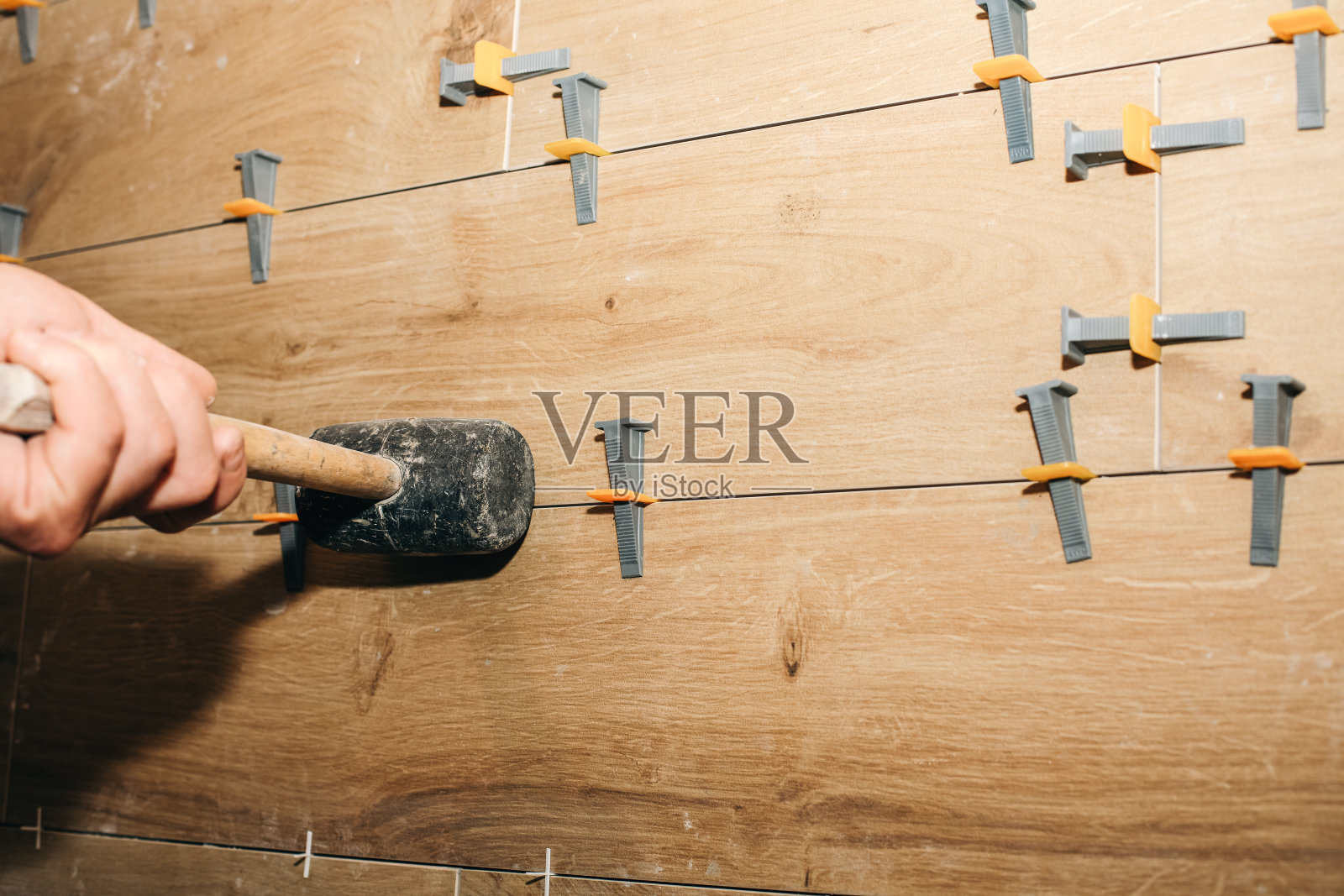 专业的瓷砖铺设。用橡胶锤放置或取出特殊的瓷砖垫片。维修保养工程装修单位。恢复在室内。工作过程。照片摄影图片