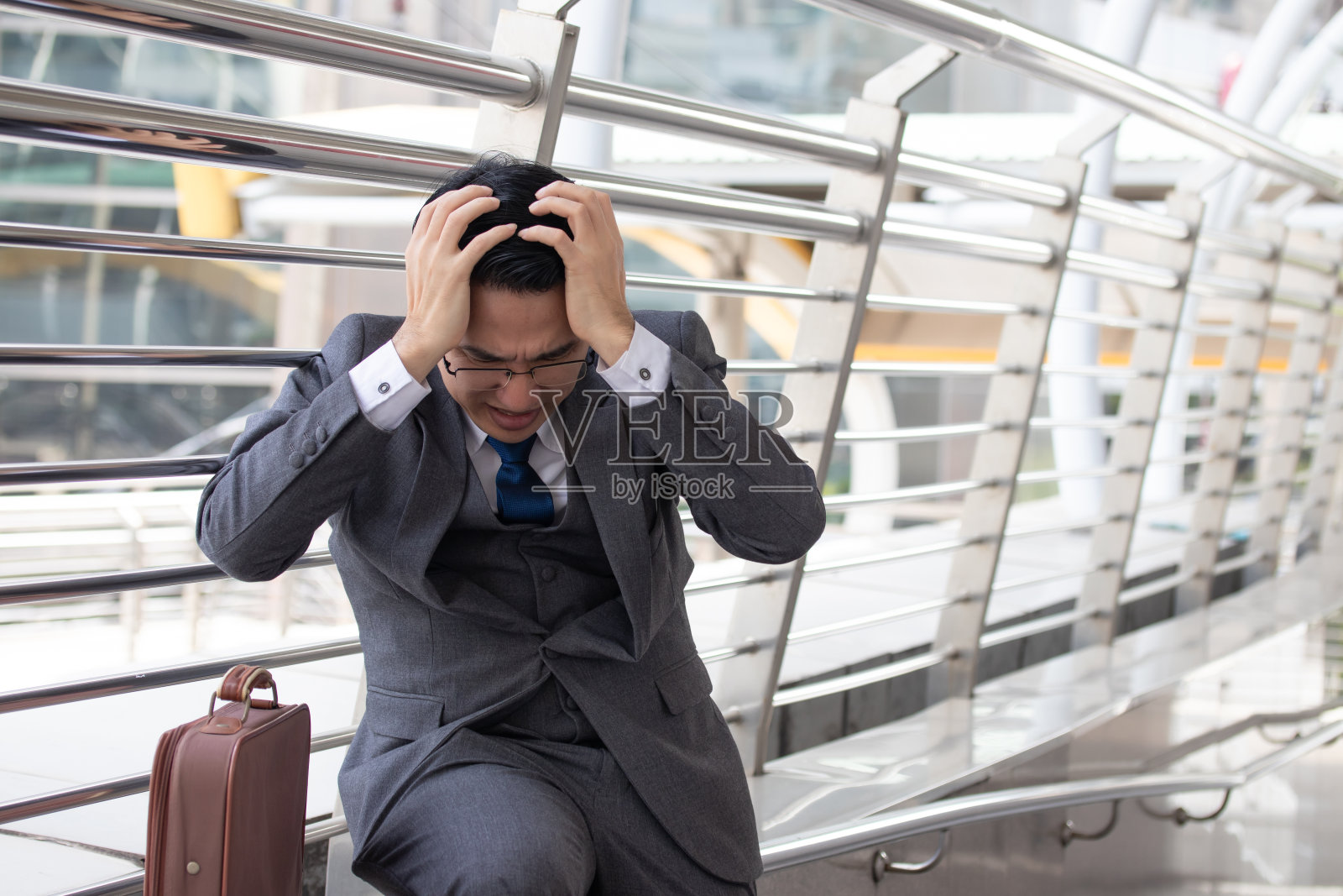 沮丧的亚洲商人穿着灰色西装坐在城市的办公室外。照片摄影图片