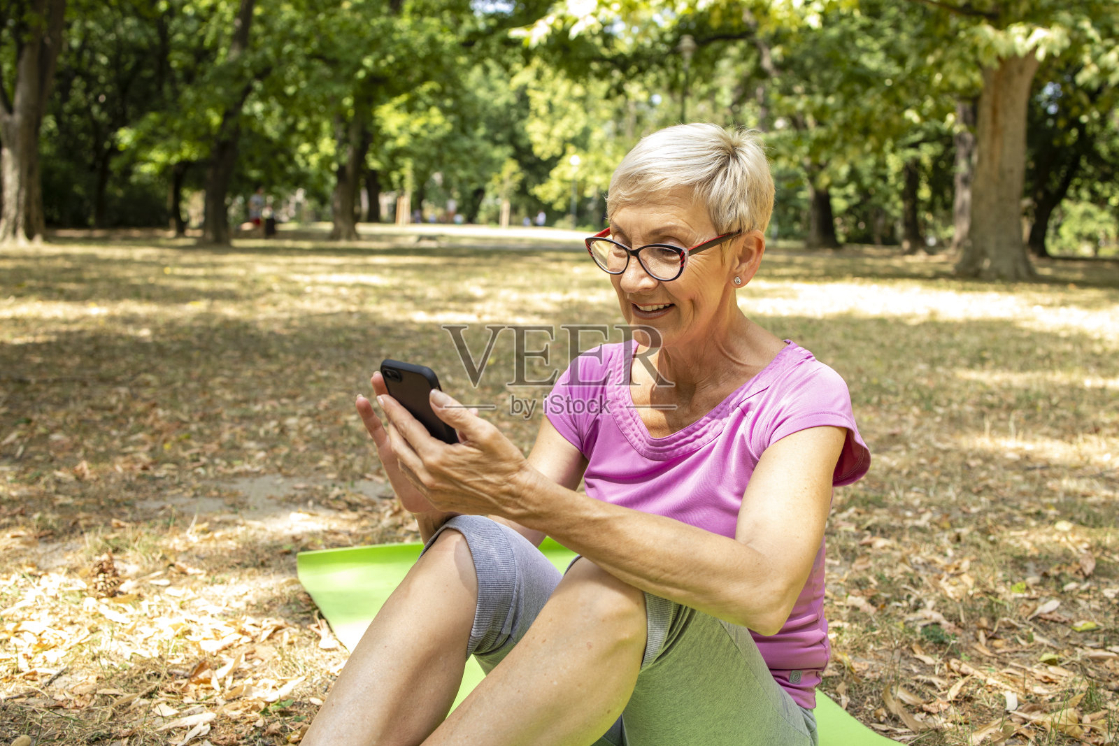 白种人老年妇女使用智能手机健康应用程序在自然中锻炼。照片摄影图片