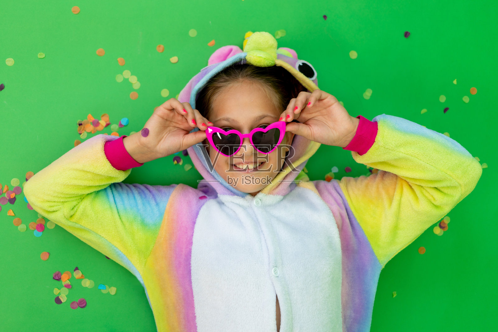 穿着鲜艳服装的小女孩们躺在绿色的孤立背景上,鲜艳的独角兽服装上挂着一条飘带。空间的文本。节日、生日和促销的概念照片摄影图片