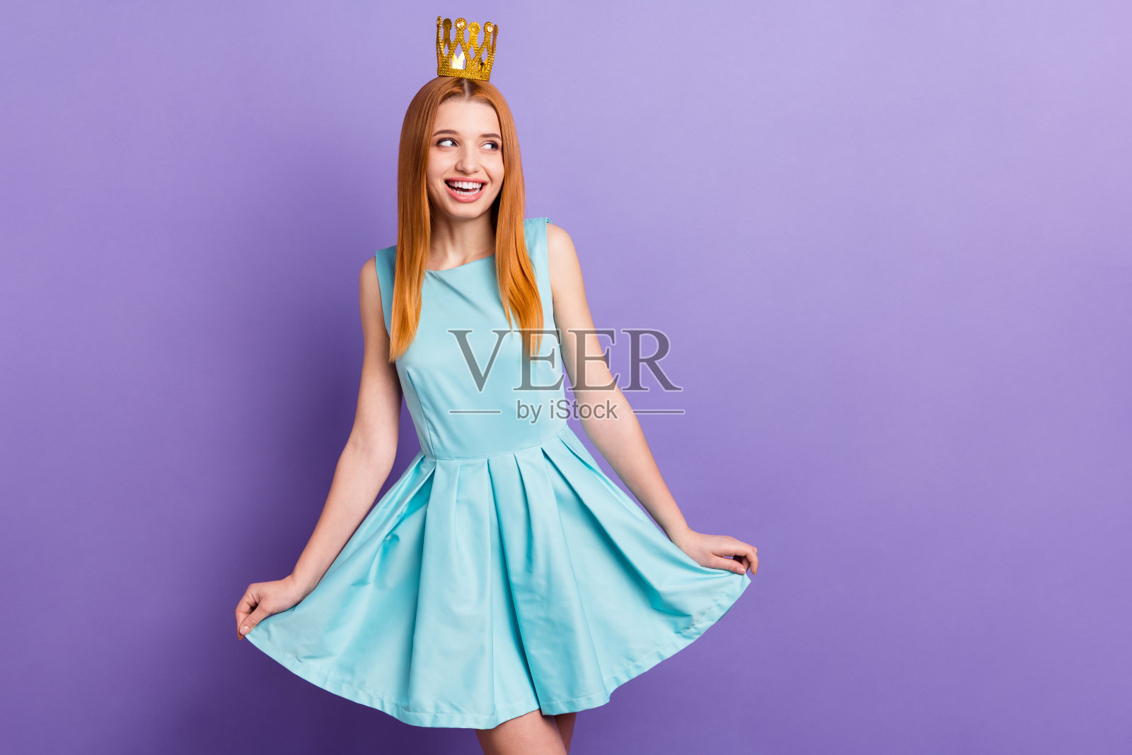 照片中的年轻迷人的女孩快乐积极的微笑戴着金色的皇冠公主孤立在紫色的背景照片摄影图片