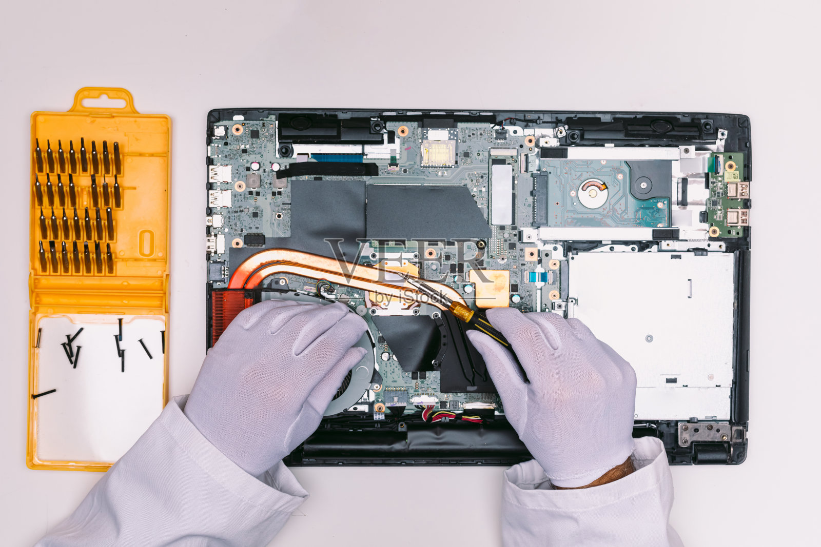 从一个戴着白手套的工程师的头上看,他正在一张白色的桌子上修理一台笔记本电脑照片摄影图片