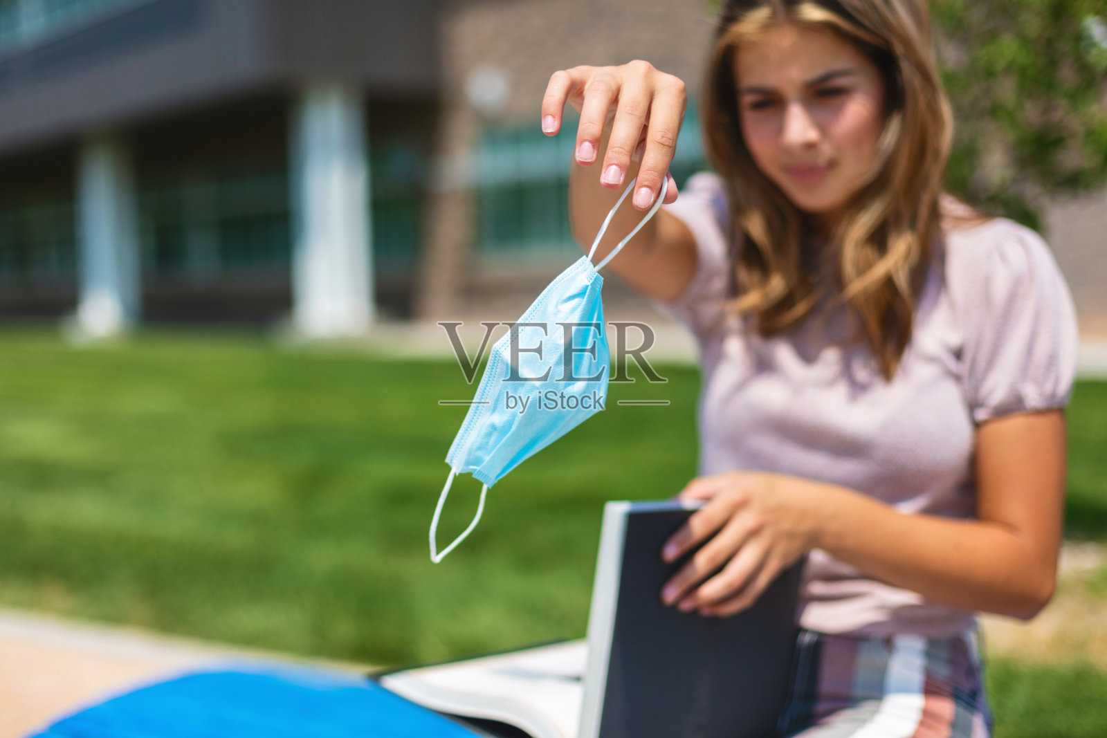 女青少年戴着口罩坐在公立学校大楼外,强制遵守重返学校照片系列照片摄影图片