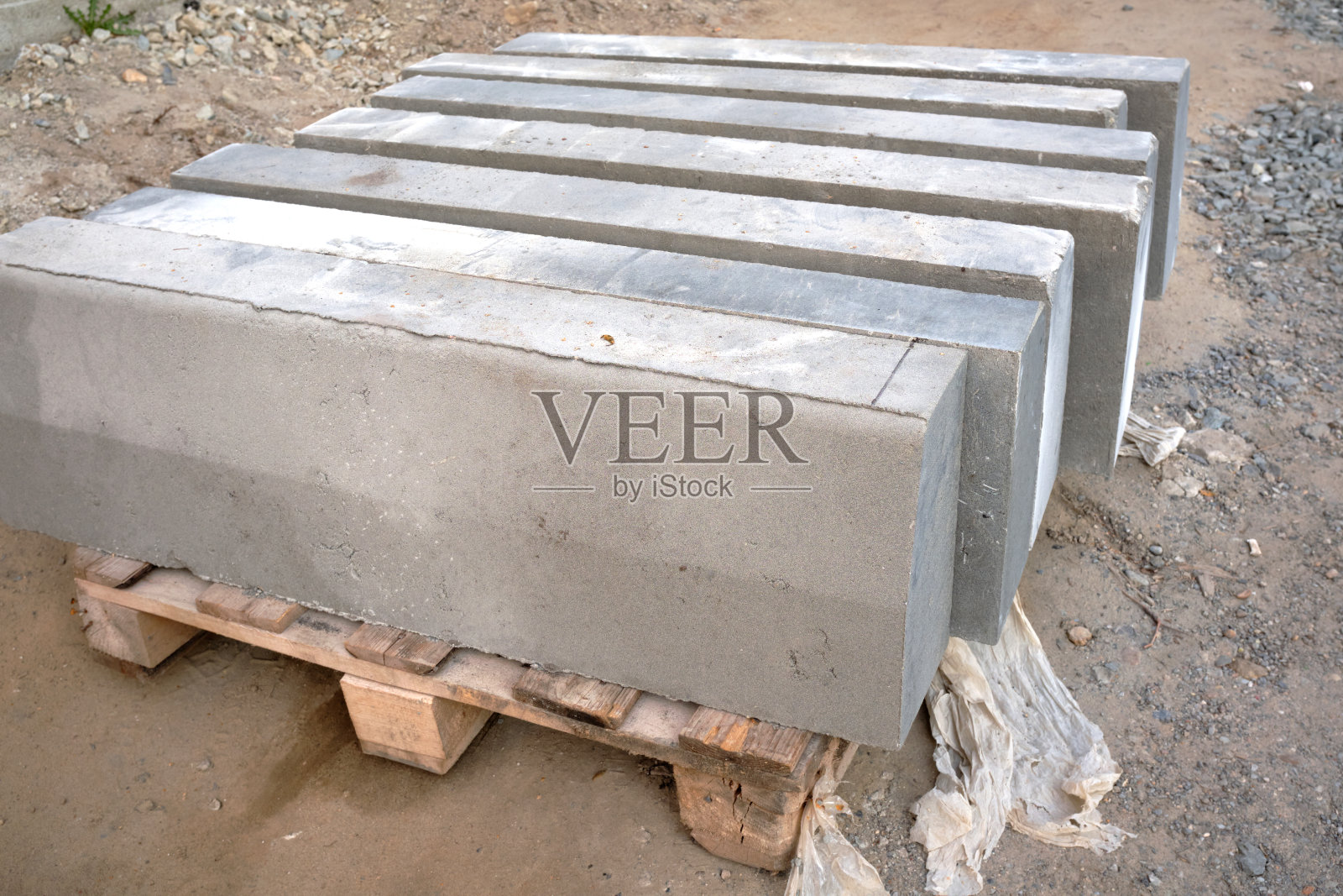 铺在人行道上的托盘上的一堆灰色的镶边石。带有混凝土路沿石的托盘。道路维修。几堆准备下蛋的路缘。照片摄影图片