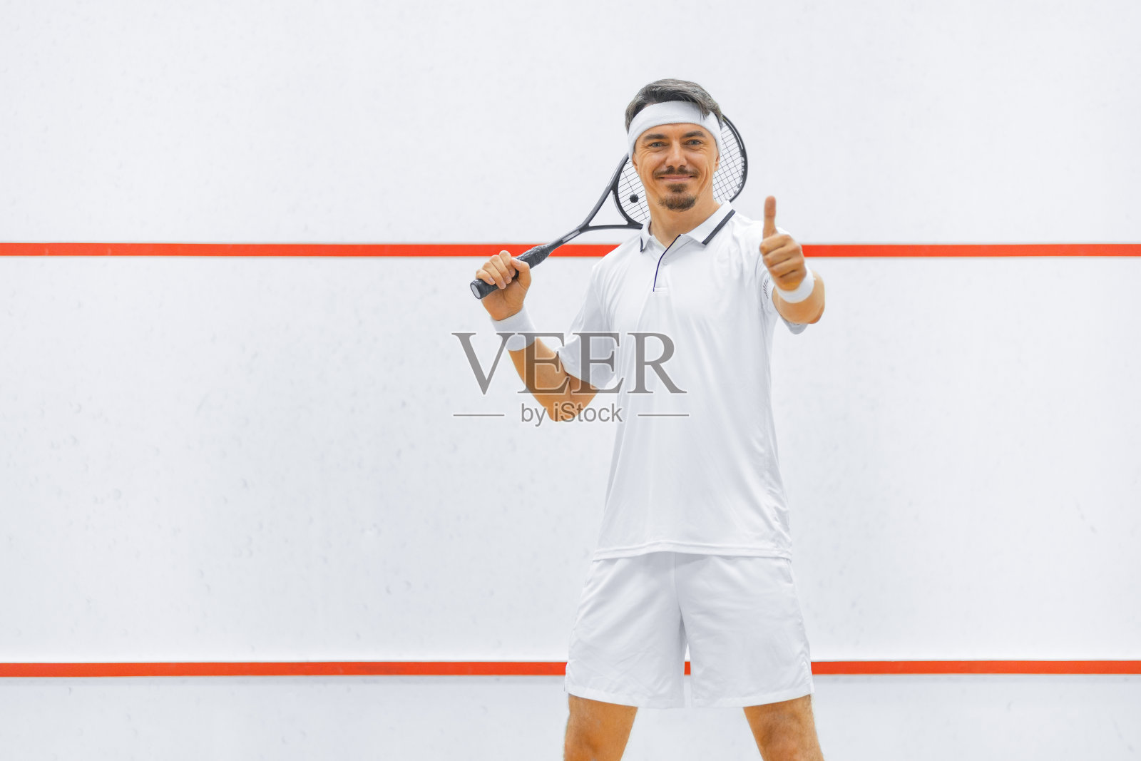 在壁球场上拿着球拍的壁球运动员。白色的运动服。照片摄影图片