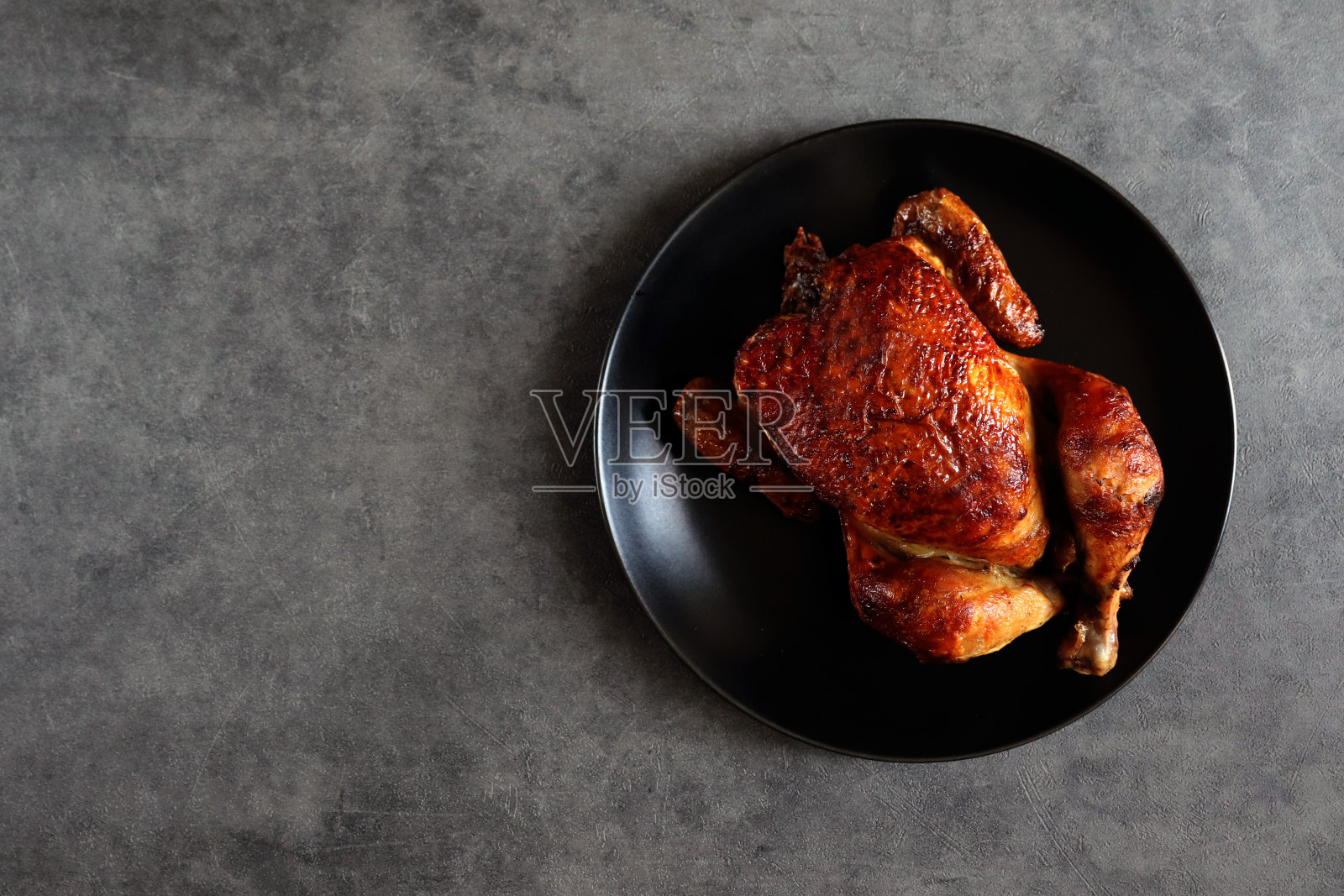 烤鸡配美味的炸皮,黑色的盘子。照片摄影图片