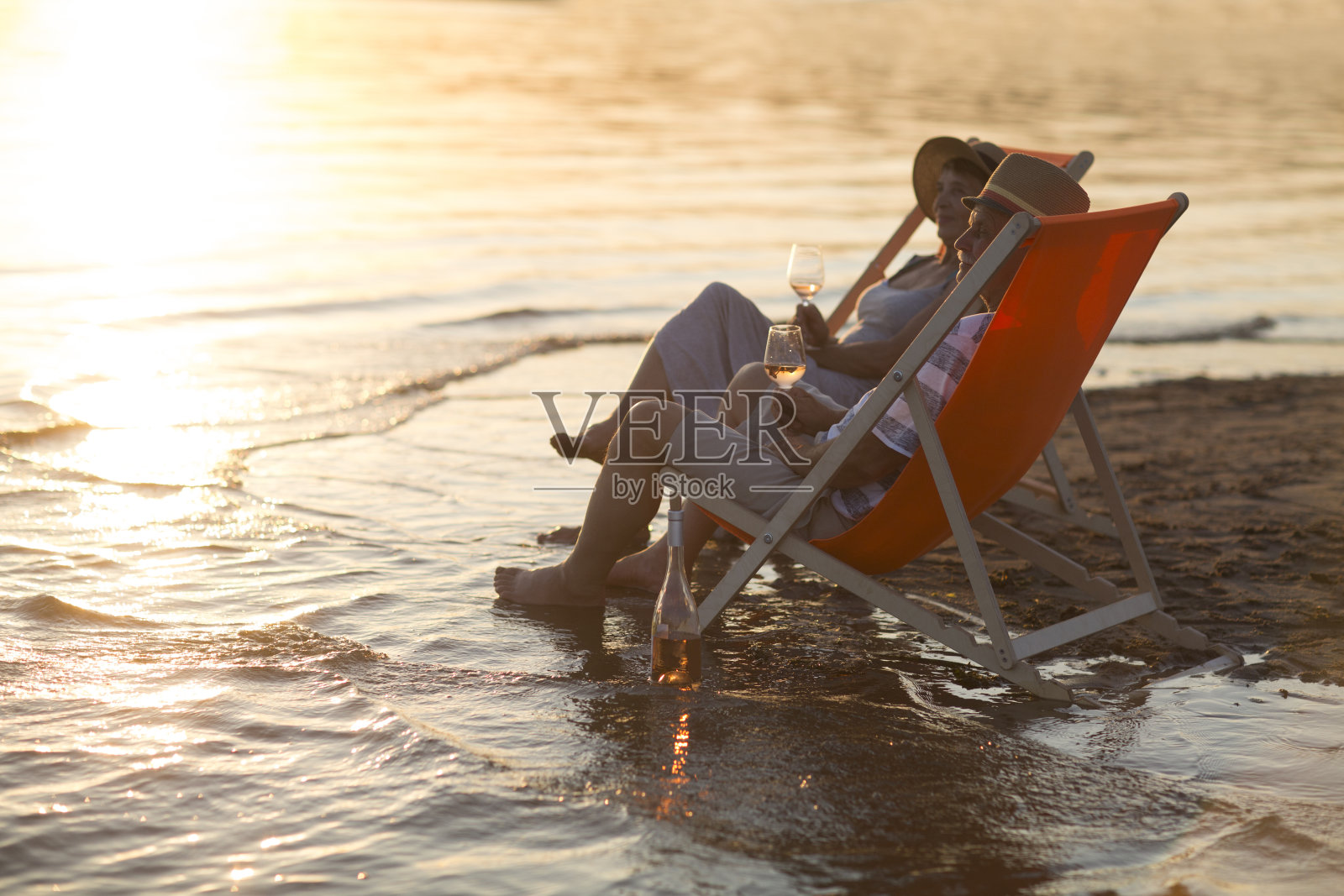 老夫妇喝着葡萄酒,在海滩上消磨时光。照片摄影图片