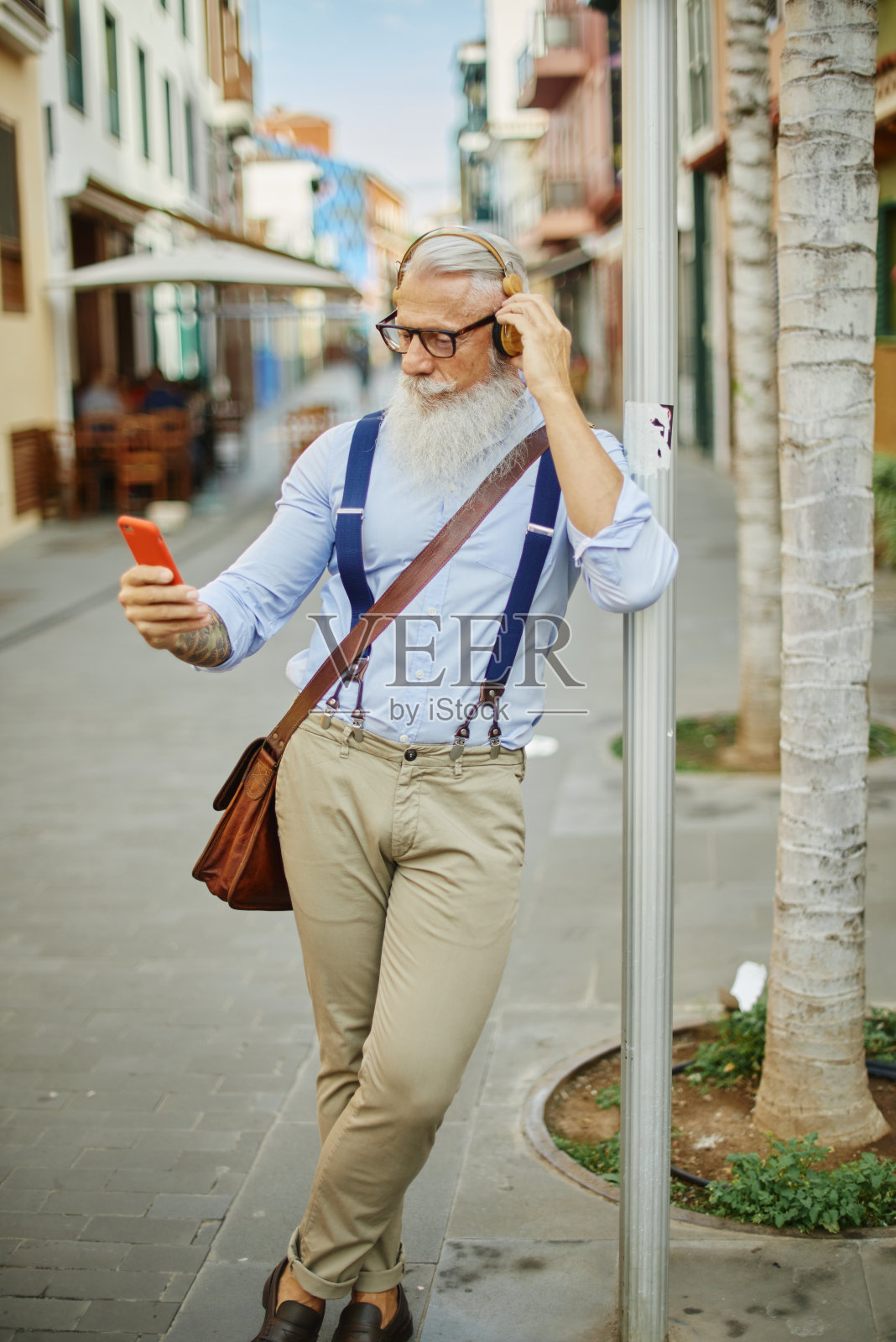 老年潮人使用智能手机,播放音乐,在紧握城市交通标志的同时享受手机技术的乐趣-快乐,科技和快乐的老年生活理念照片摄影图片