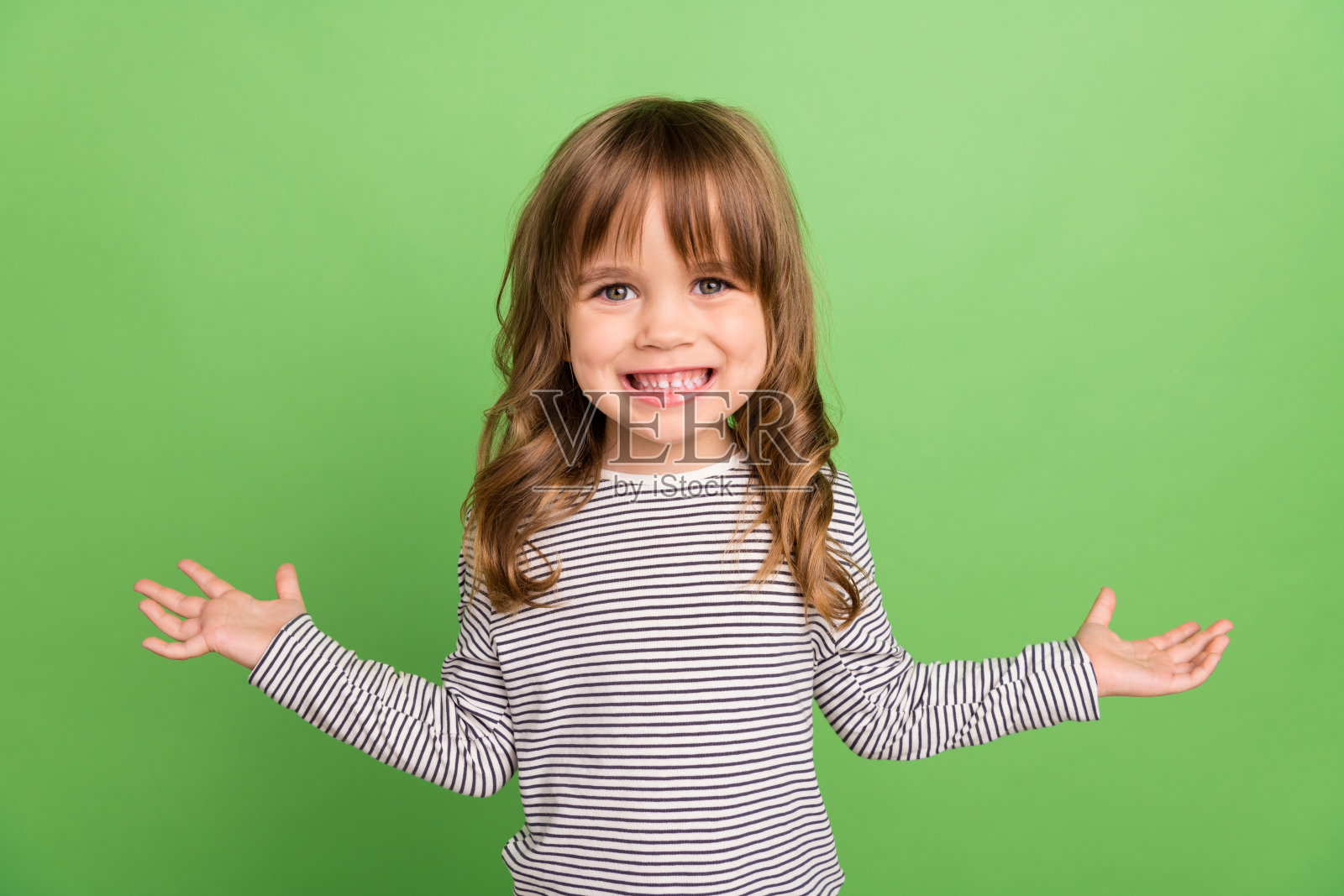 照片中有趣的金发小女孩双手拥抱穿着条纹衬衫孤立在绿色背景上照片摄影图片