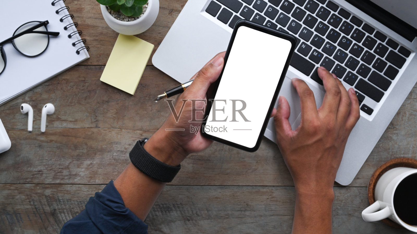 一名男子拿着智能手机,在工作场所用笔记本电脑工作。照片摄影图片