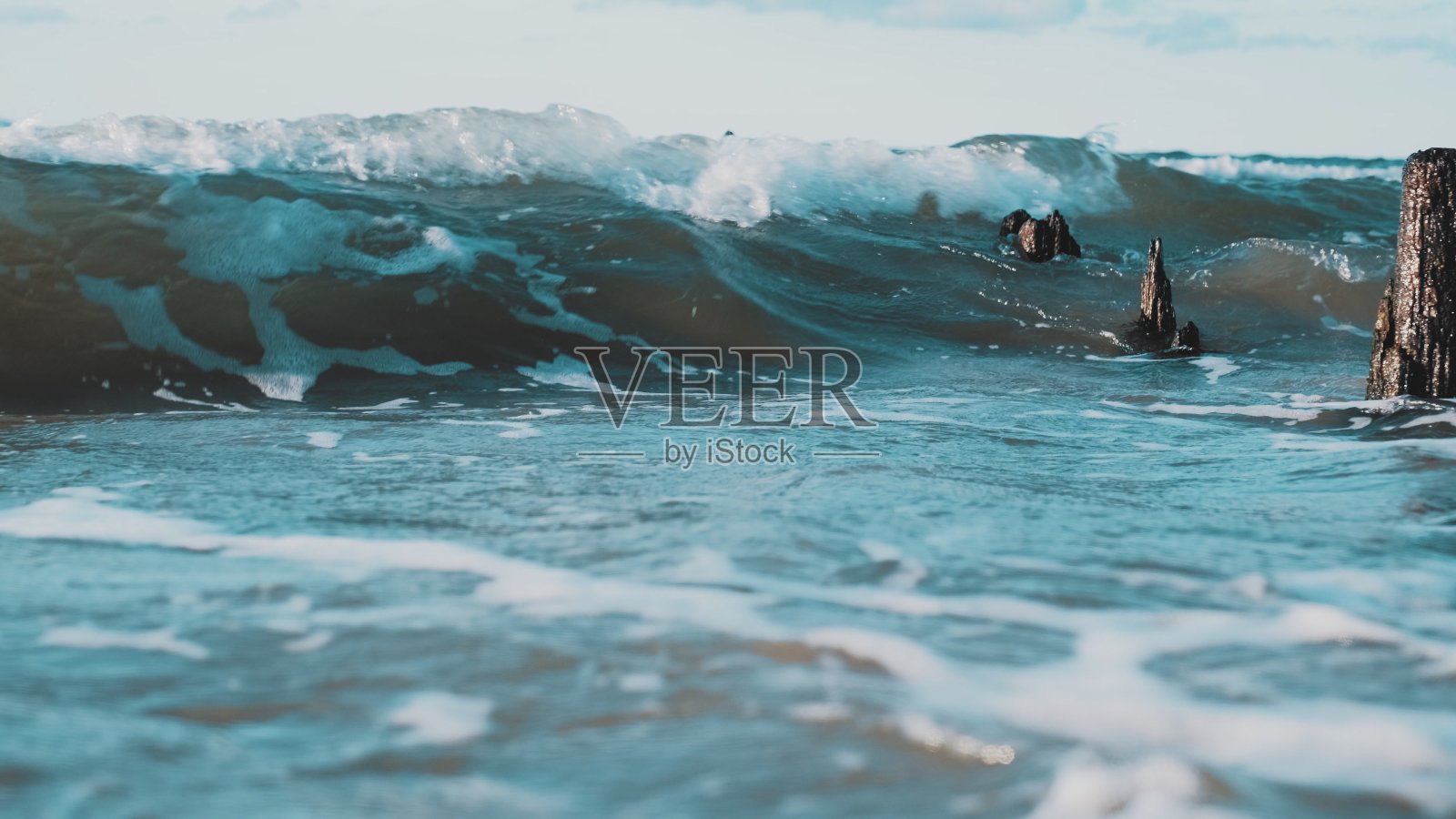 海浪在老旧的、枯萎的、腐烂的、被侵蚀的木防波堤杆上破碎照片摄影图片