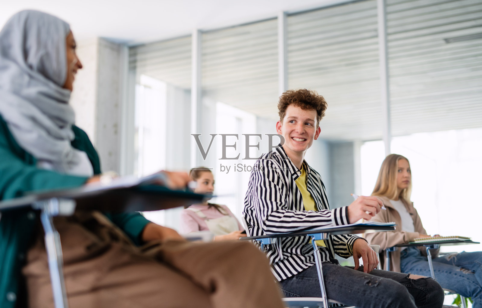 一幅大学生坐在教室里学习的画像。照片摄影图片
