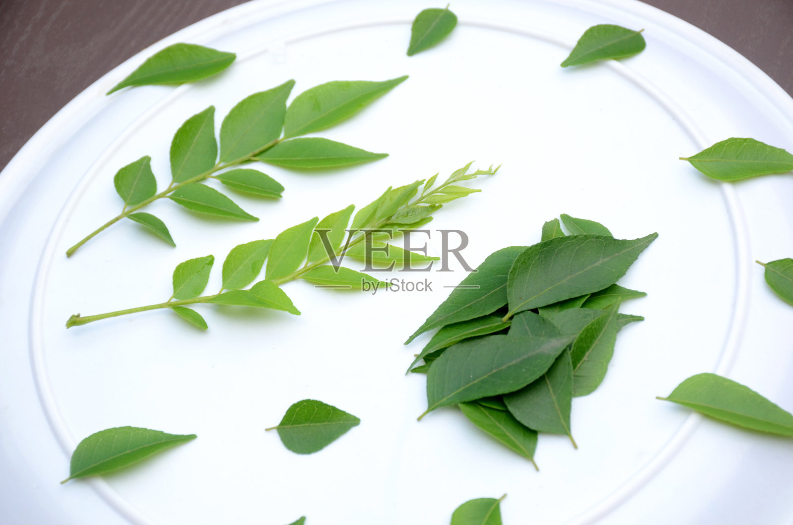 将一束绿色的咖喱叶放在白色的盘子上,背景是棕色的。照片摄影图片