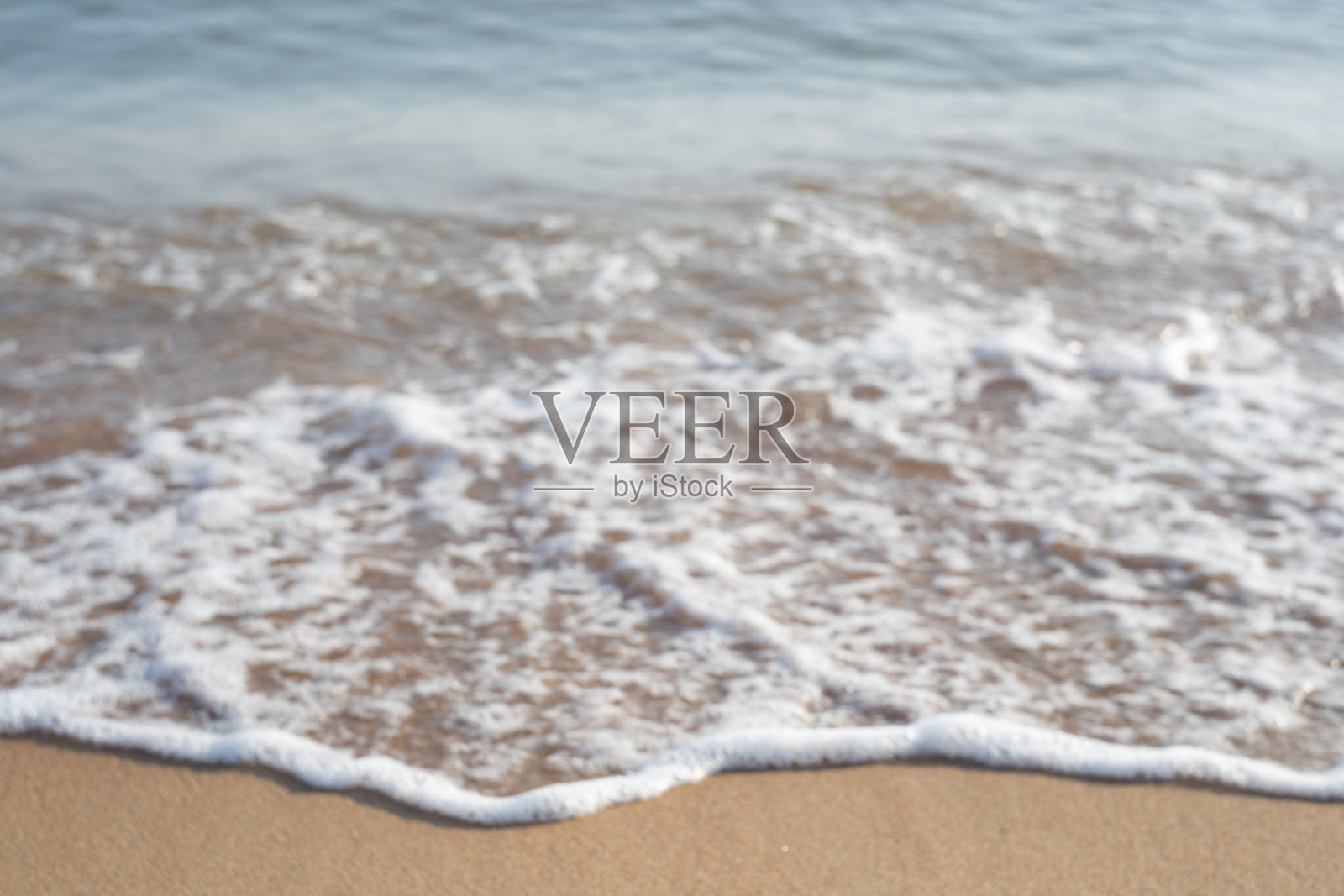 模糊的中性海岸背景。海浪打在沙滩上,溅起泡沫照片摄影图片